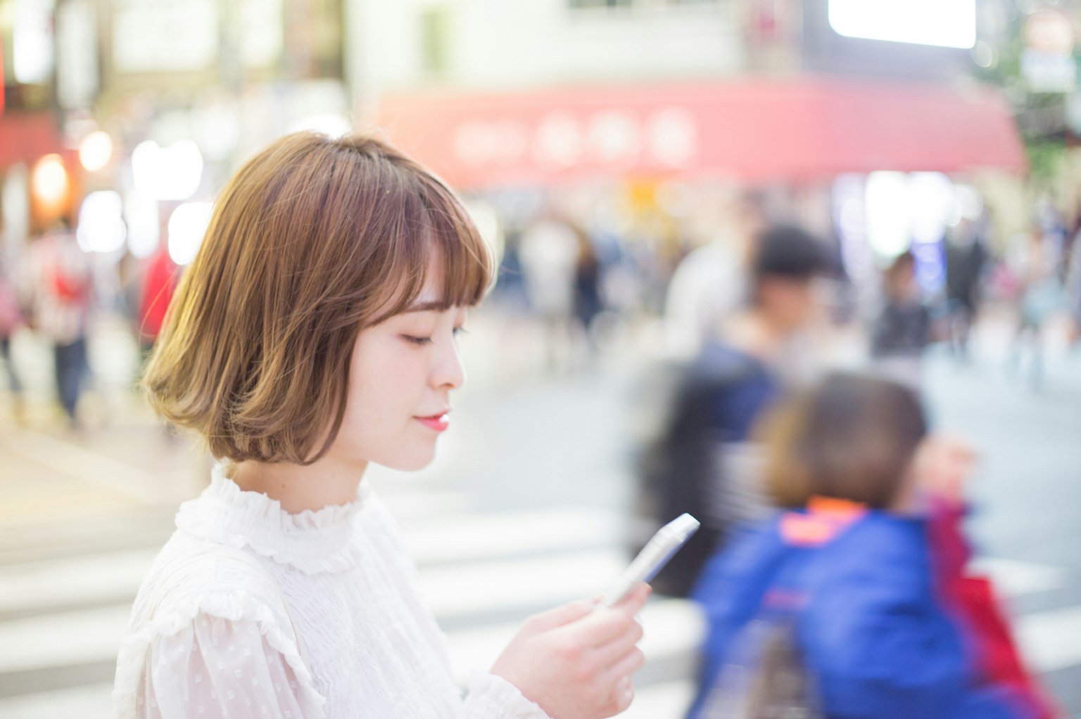 Young woman looking at smartphone in a busy street scene with blurred background