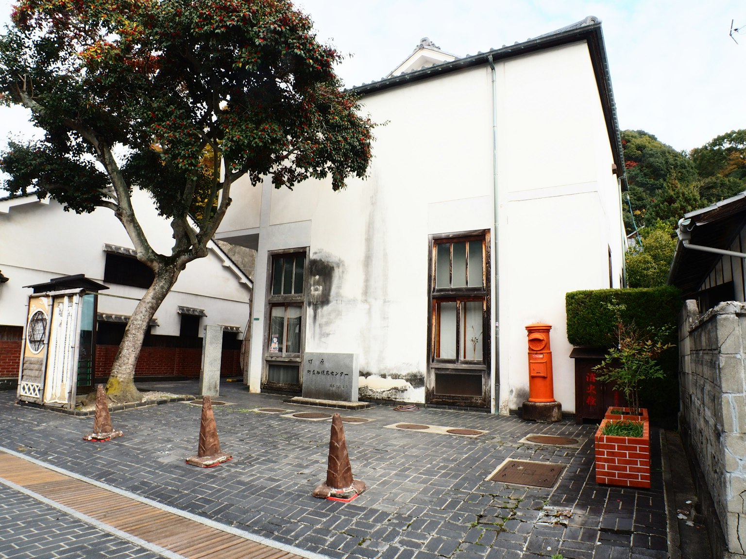 Un edificio bianco con grandi alberi e una cassetta postale rossa su un sentiero in ciottoli