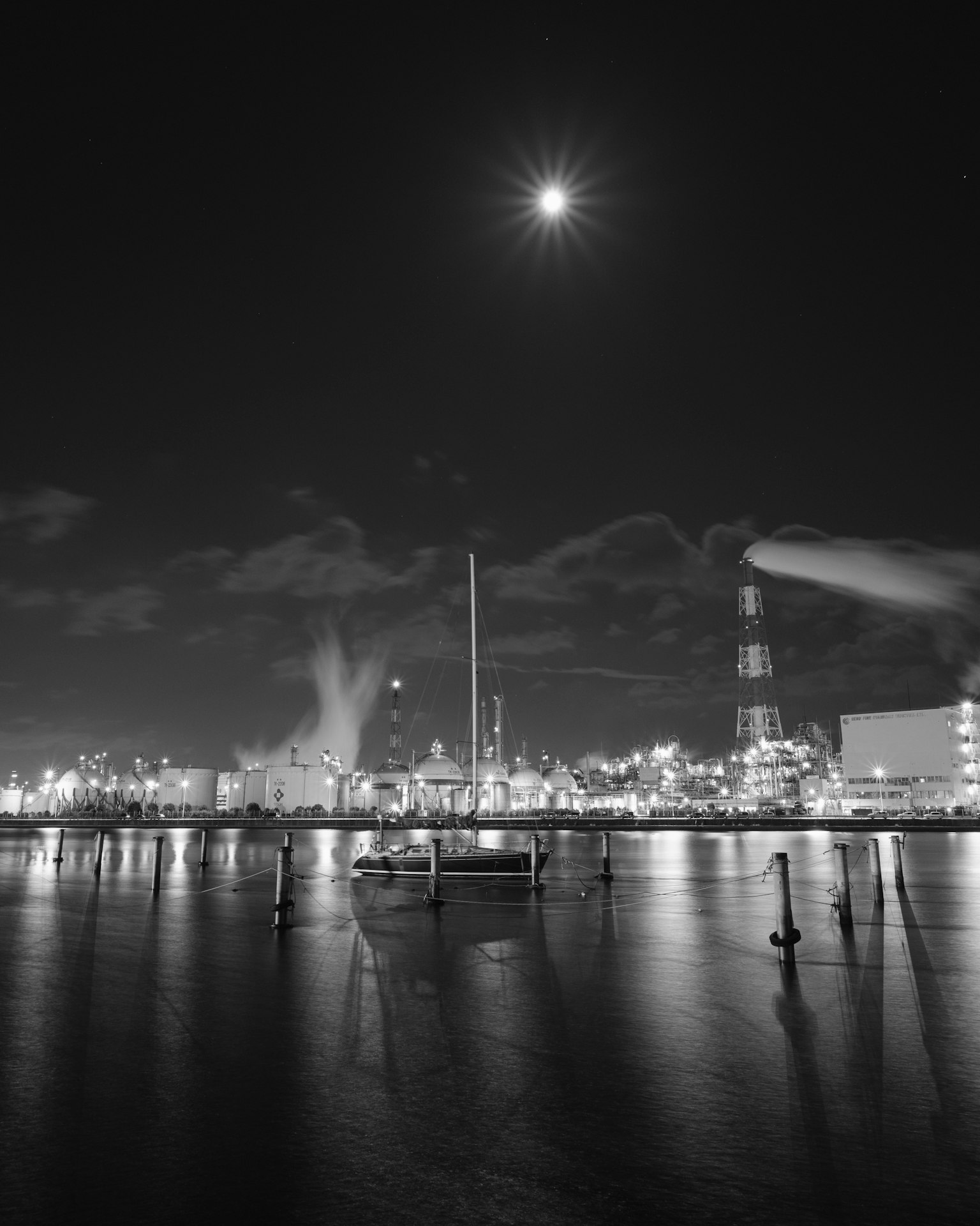 Night view of an industrial area with a moon and reflections on the water