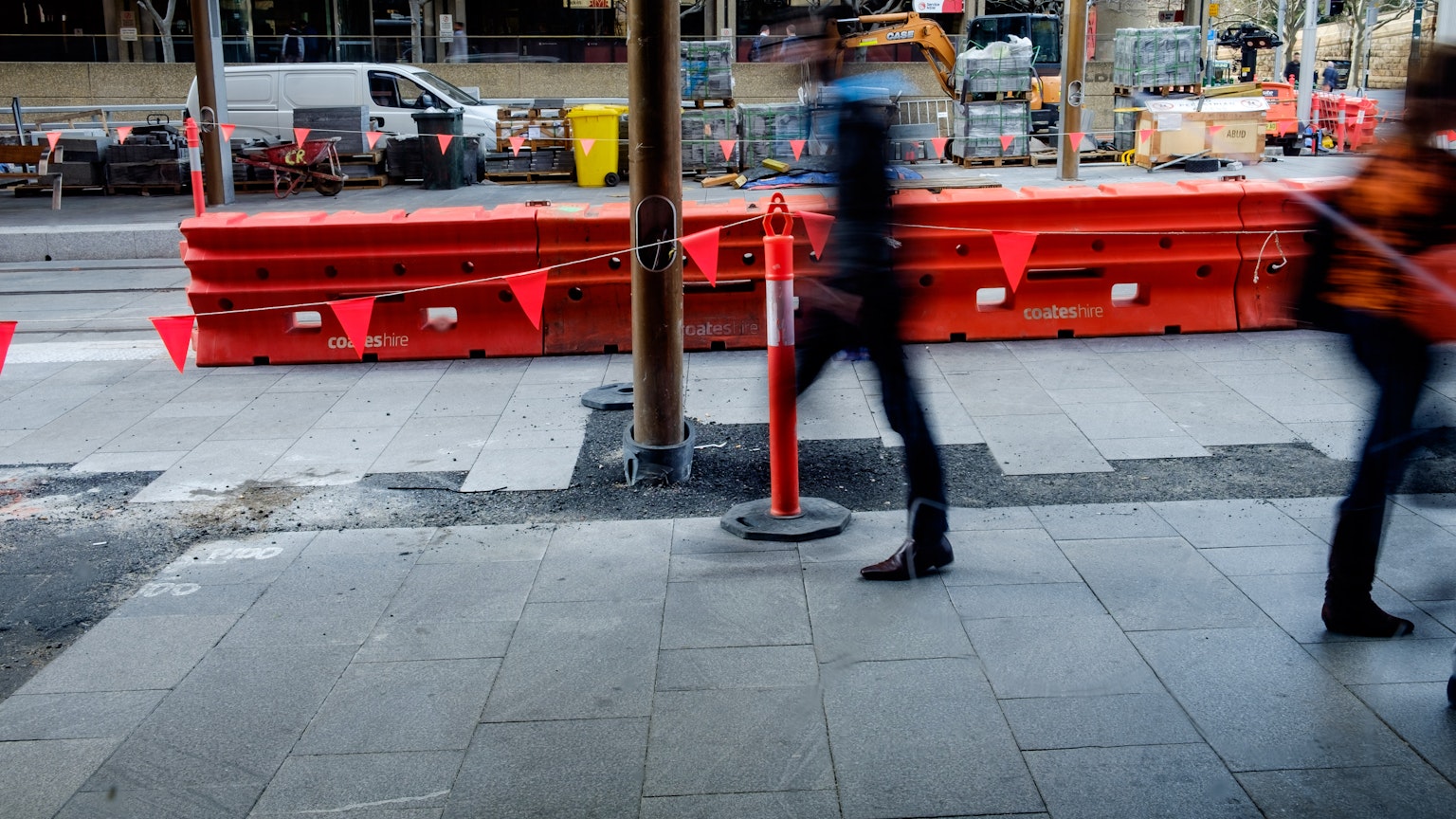 Immagine di persone che camminano accanto a barriere rosse e un cantiere sul marciapiede