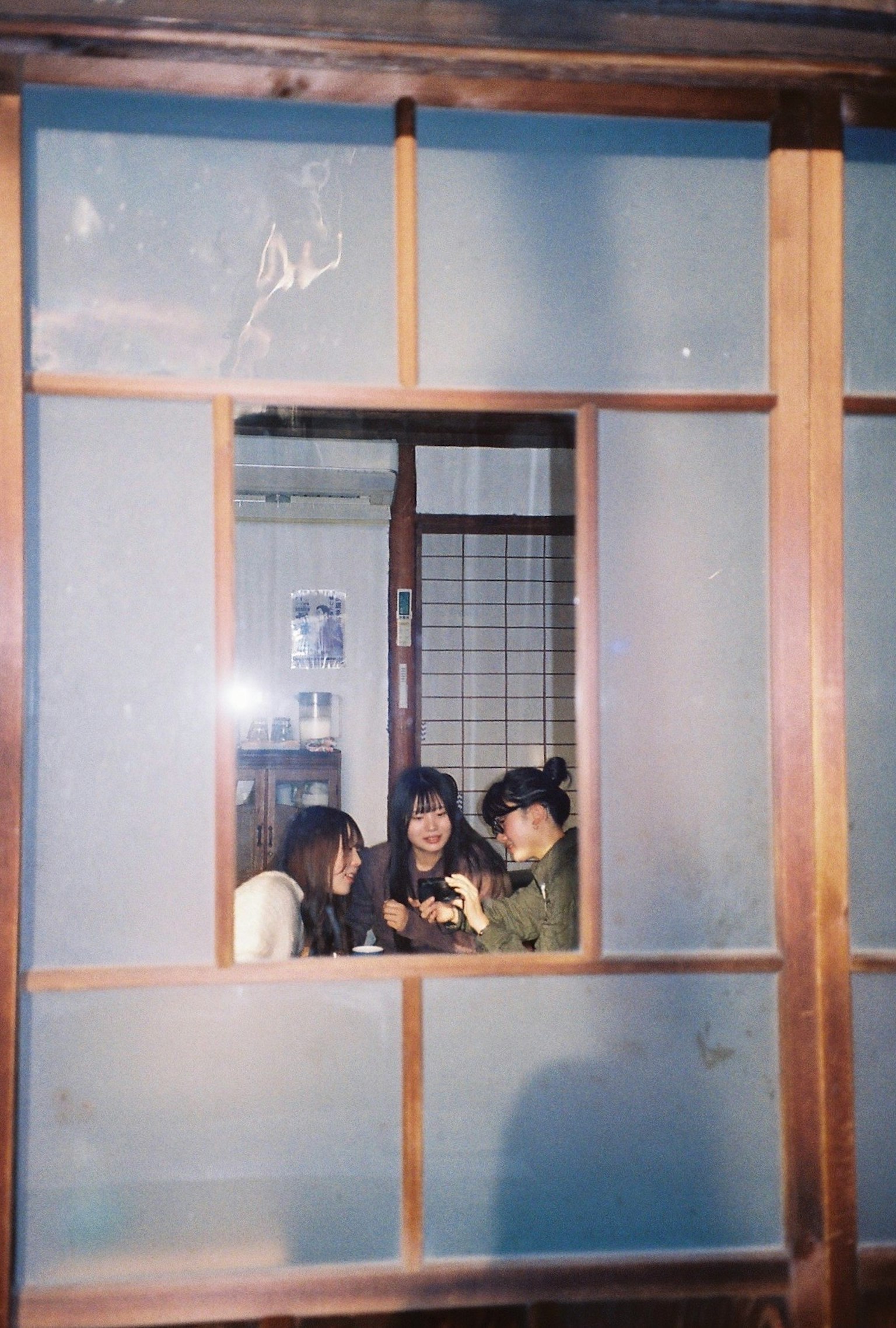 Three women engaged in conversation seen through a wooden window frame
