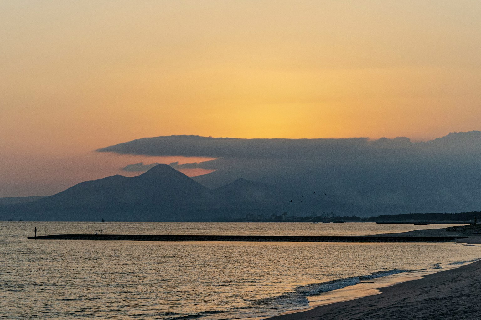 Pemandangan pantai saat matahari terbenam dengan gunung dan awan