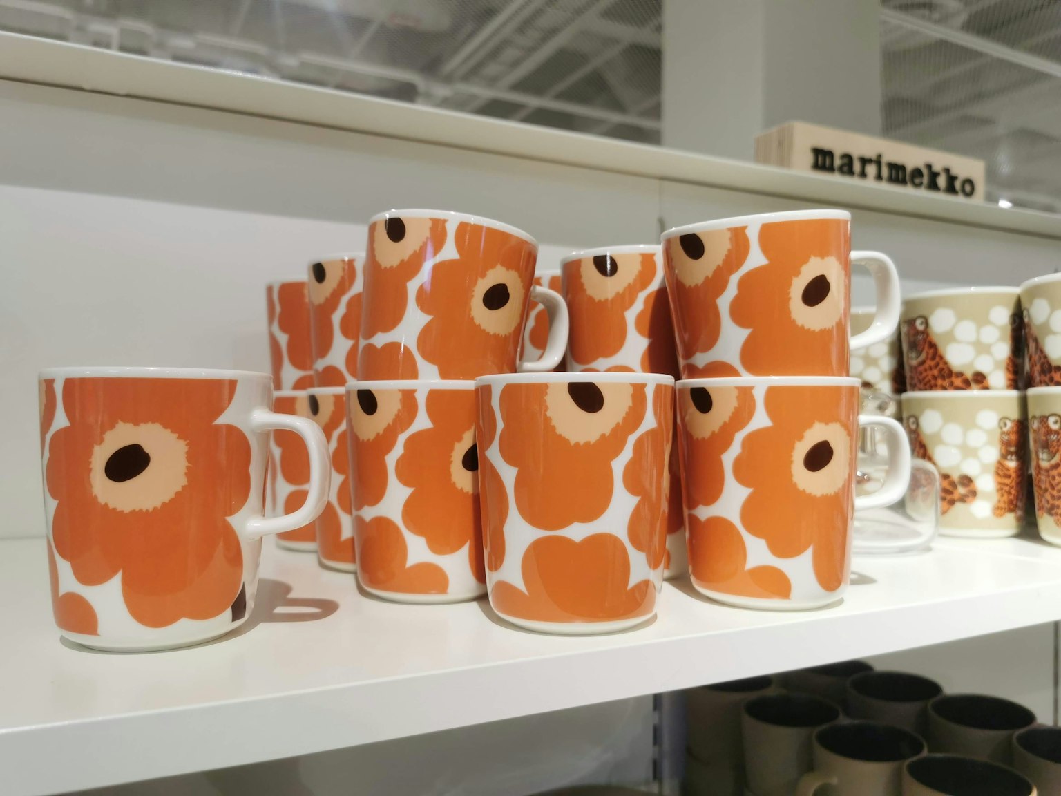 Stapel orangefarbener Marimekko-Becher mit Blumenmuster auf einem Regal