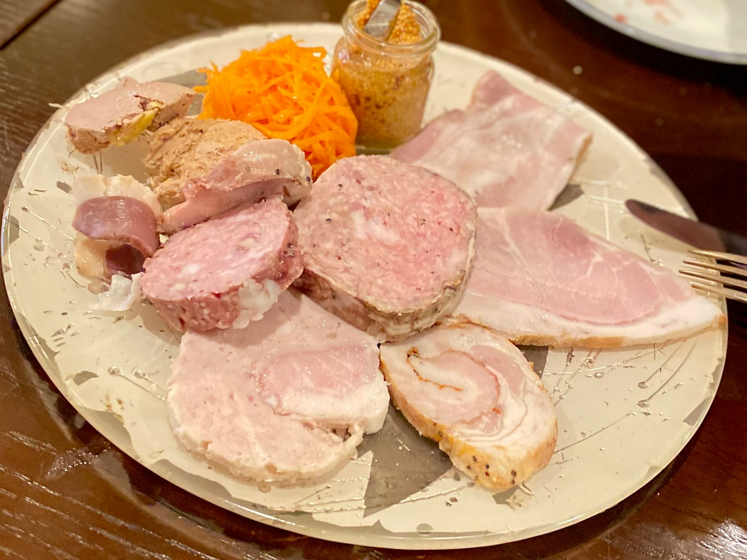 A plate featuring various types of ham and meat products accompanied by carrot salad and mustard