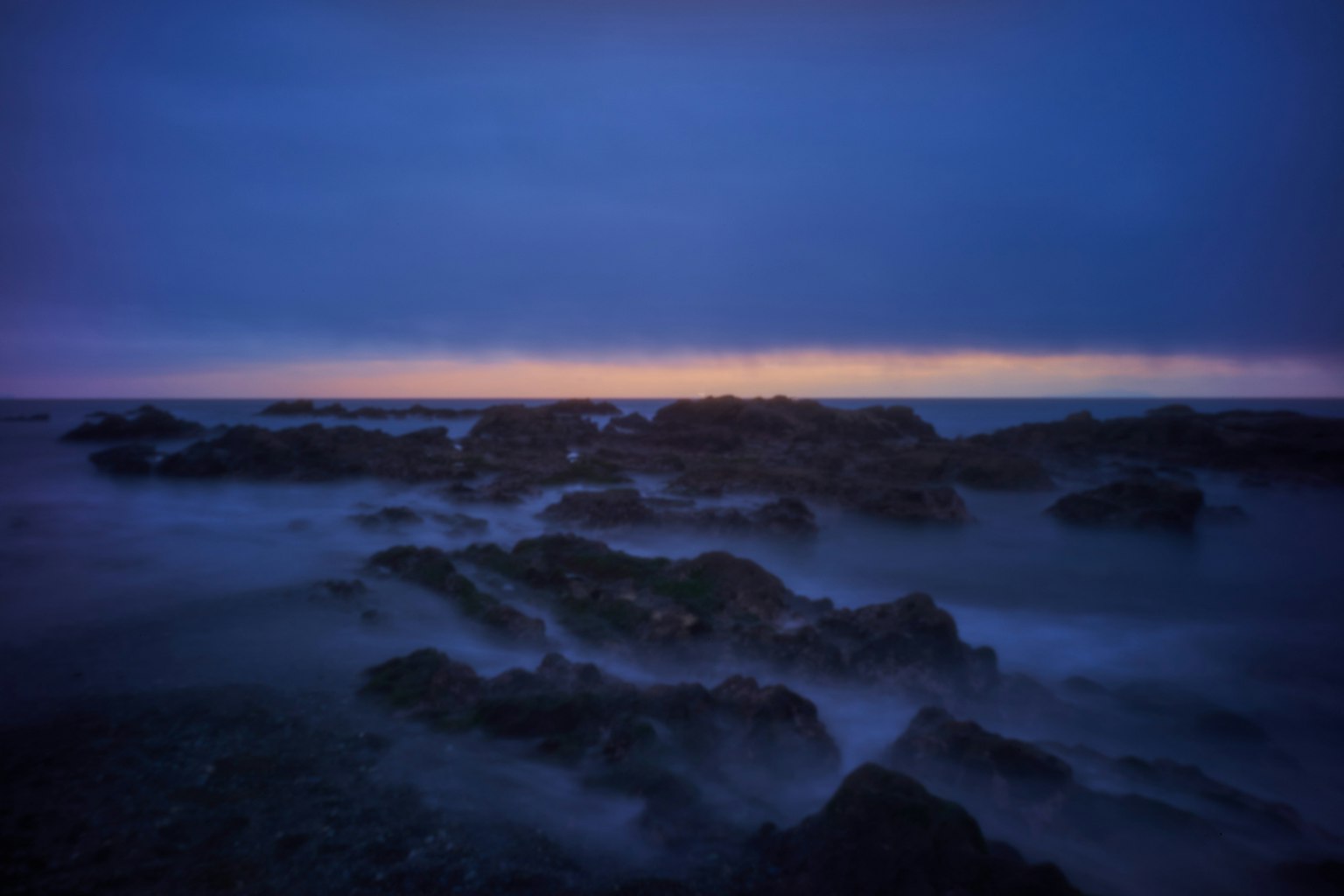 Twilight scene of rocky beach with deep blue waters and soft horizon glow