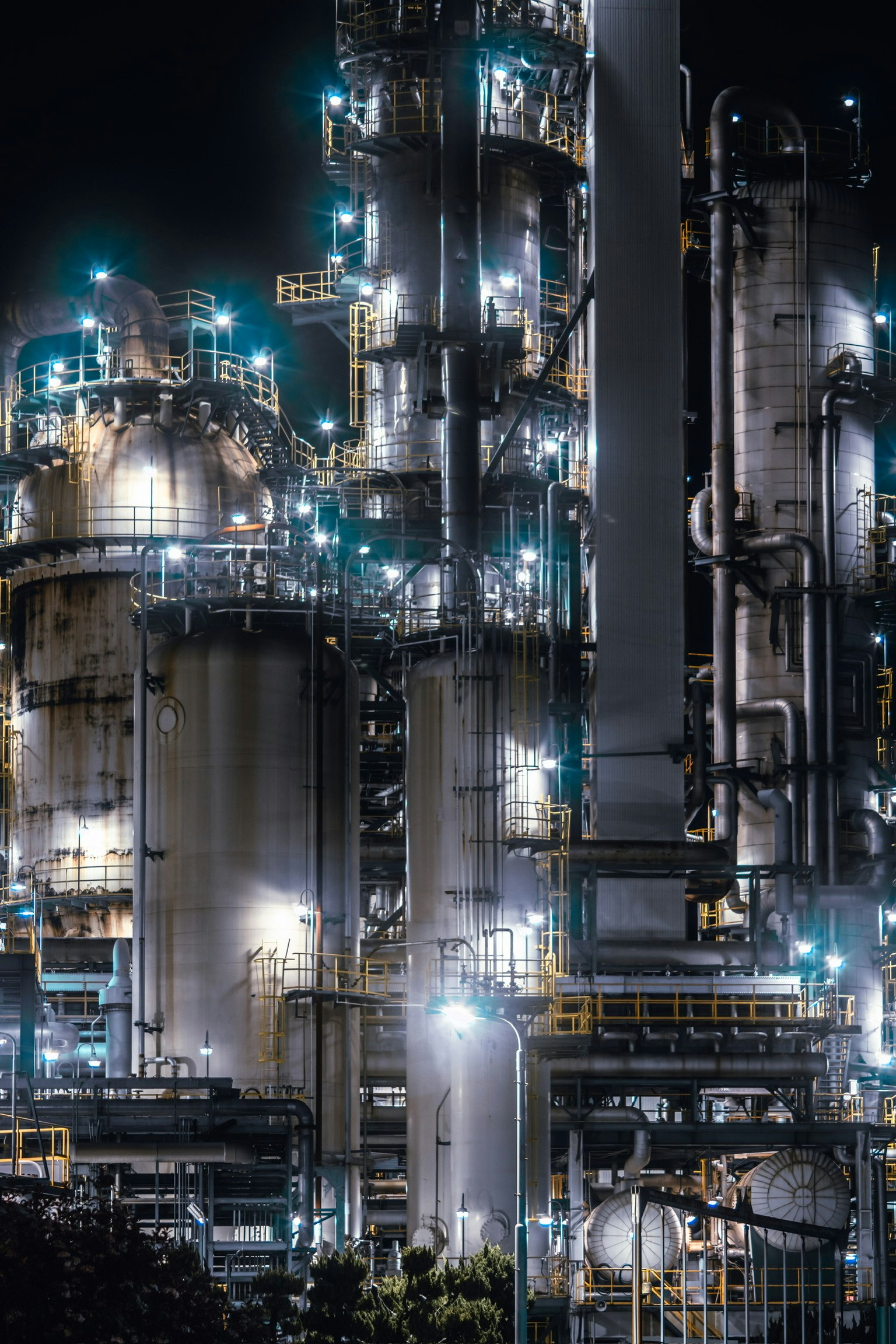 夜の工業プラントの詳細な画像 高いタンクとパイプが明るい光で照らされている