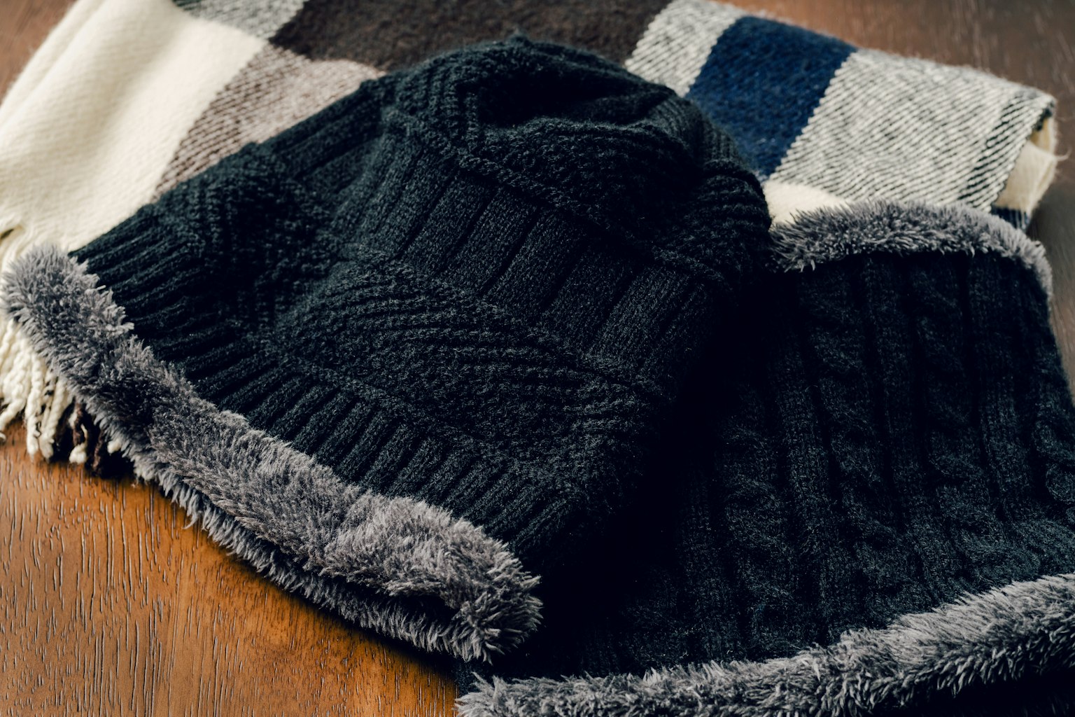 Schwarze Strickmützen und ein Schal angeordnet als warme Winteraccessoires