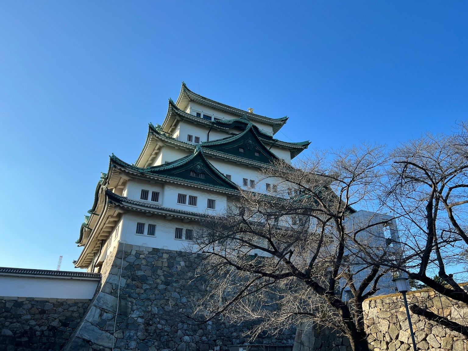 Nagoya Castle erhebt sich gegen einen klaren blauen Himmel mit Kirschbäumen