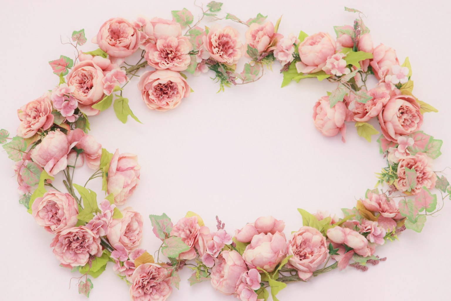 A delicate pink rose wreath arranged on a white background