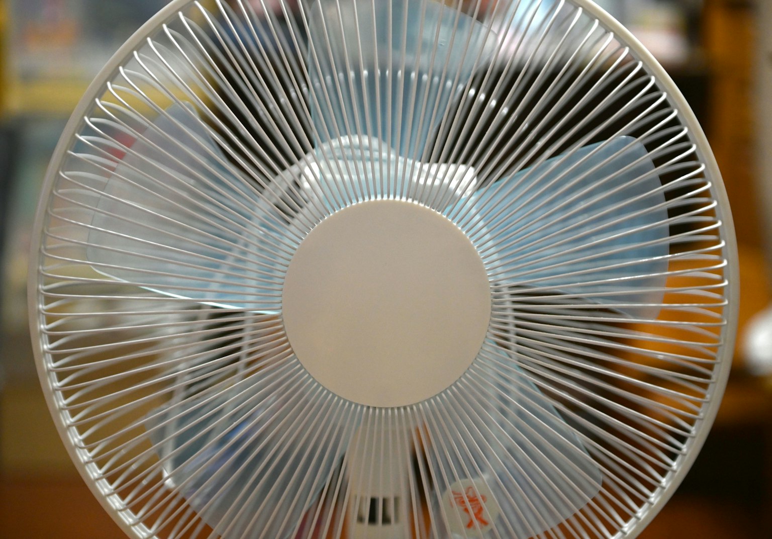 透明な扇風機の前面が見える背景にはぼんやりした色合いの物体がある