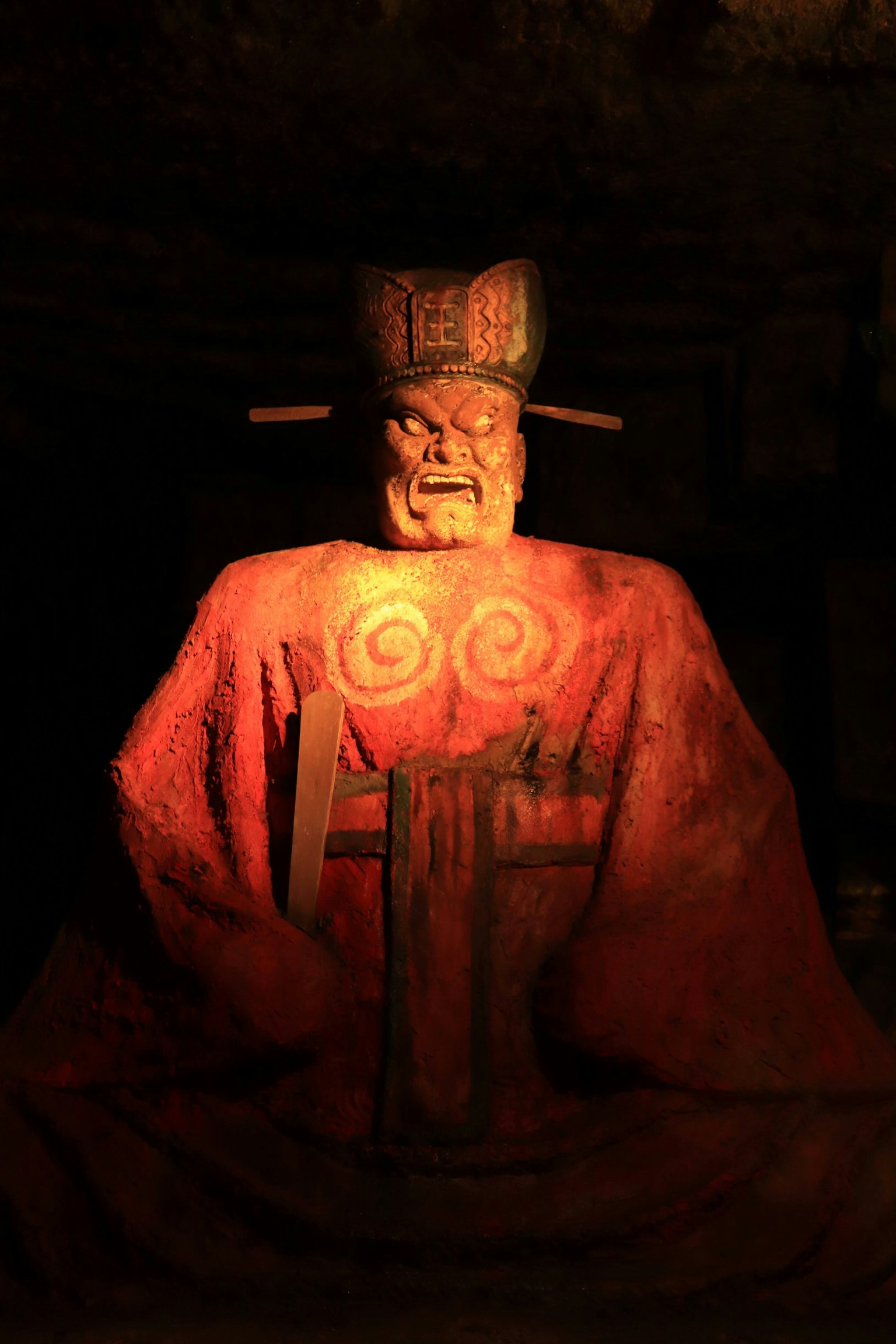赤い衣装を着た古代の彫像が暗い空間に座っている
