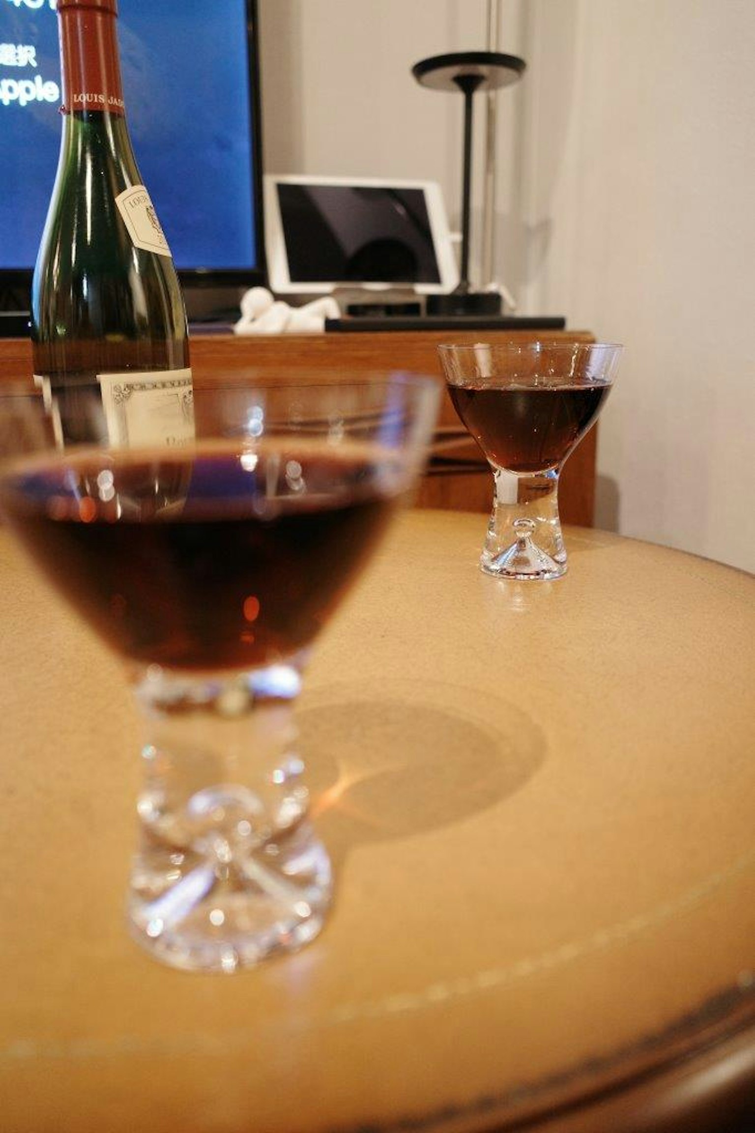 桌上放著兩個裝有深色飲料的水晶杯，背景有一瓶酒