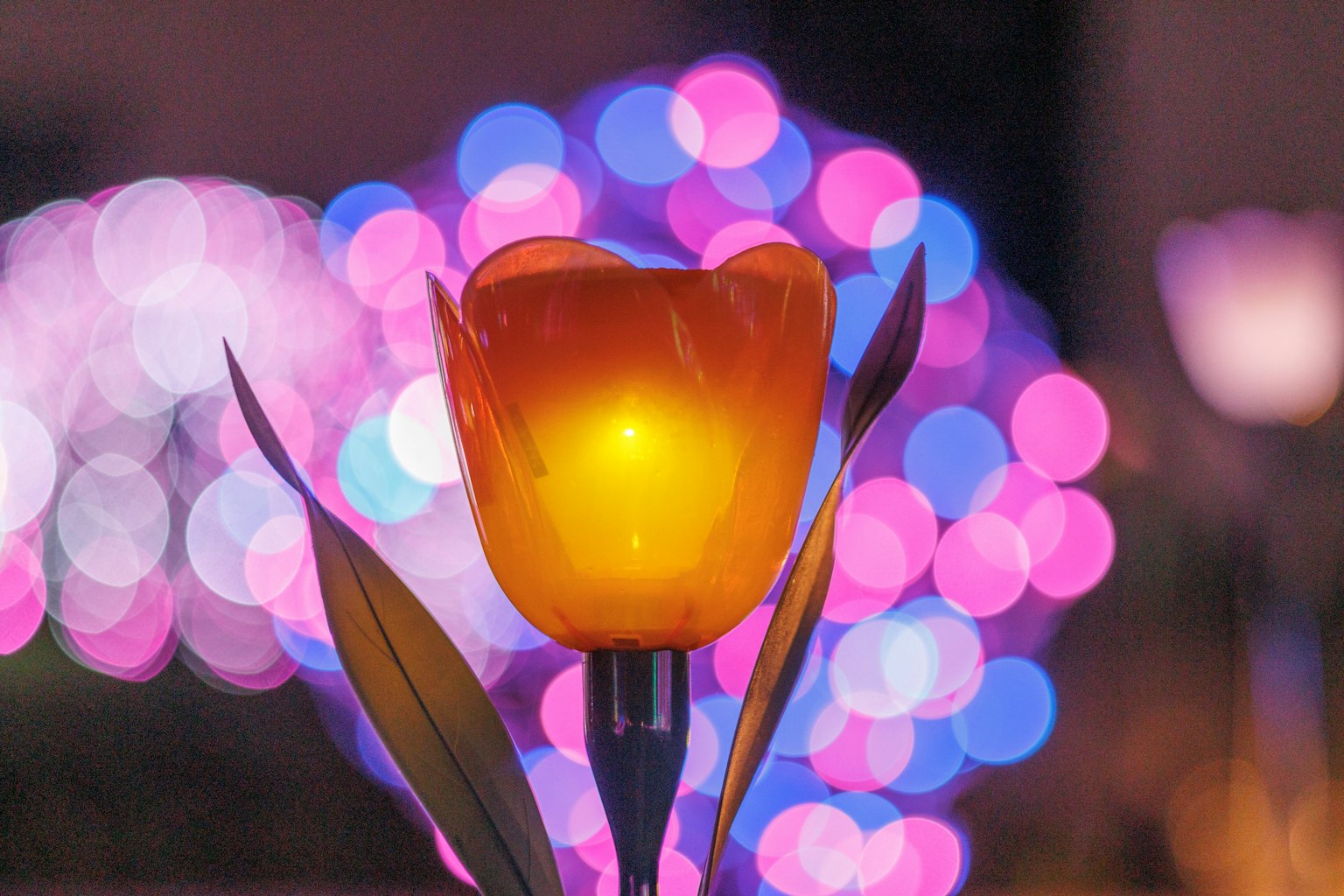 Orange tulip-shaped lamp in the foreground with colorful bokeh lights in the background
