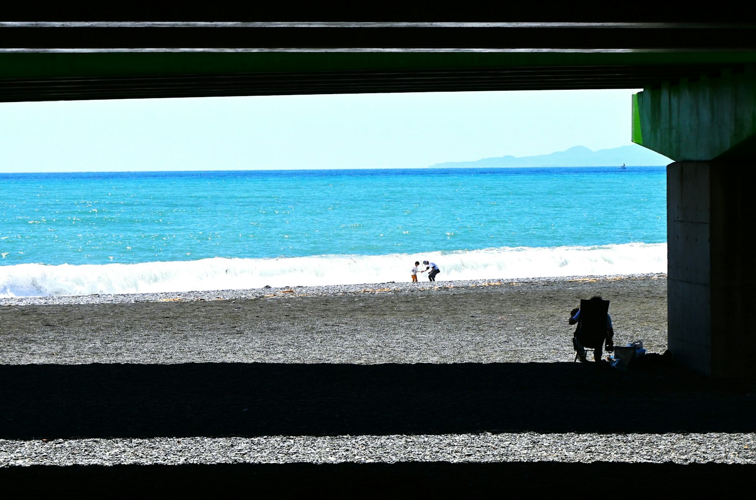 Menschen an einem Strand mit blauem Ozean und Wellen, sichtbar unter einer Struktur