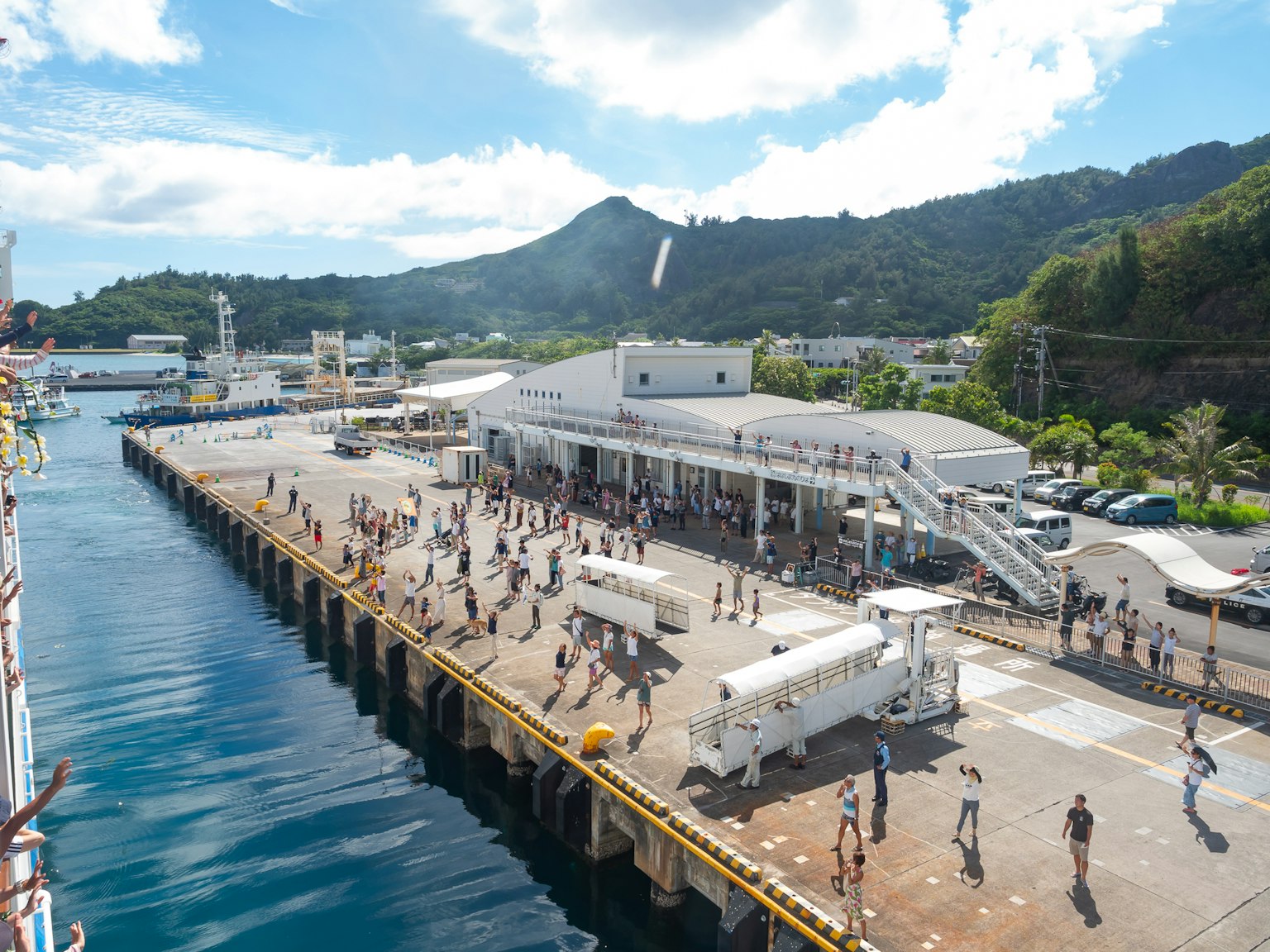 Foule rassemblée au port avec des montagnes pittoresques en arrière-plan