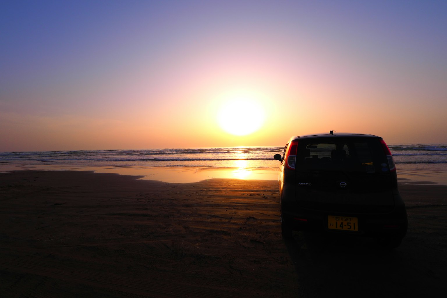 Coche negro en silueta contra un atardecer en la playa