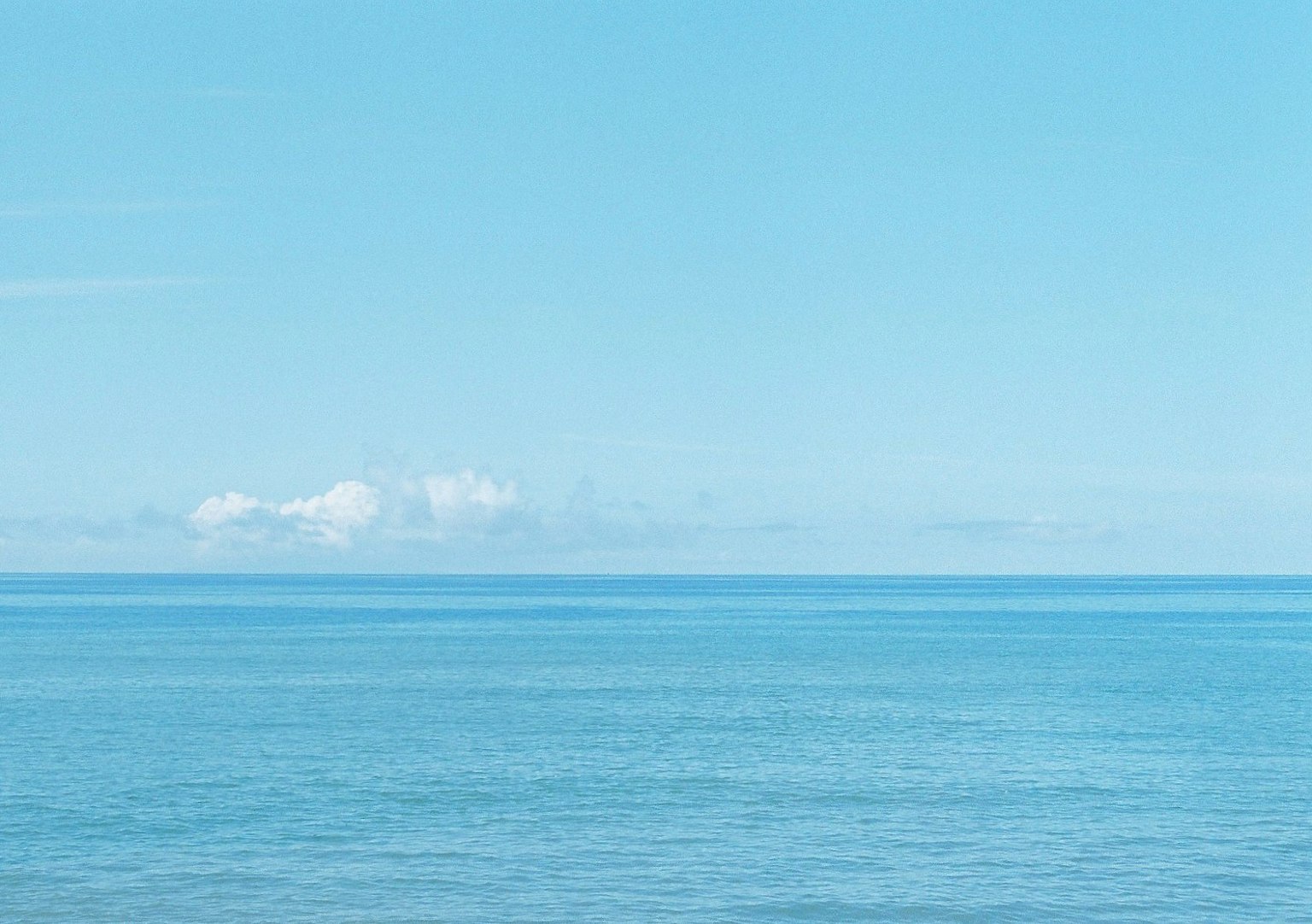 Pemandangan tenang laut biru dan langit dengan gelombang lembut dan awan
