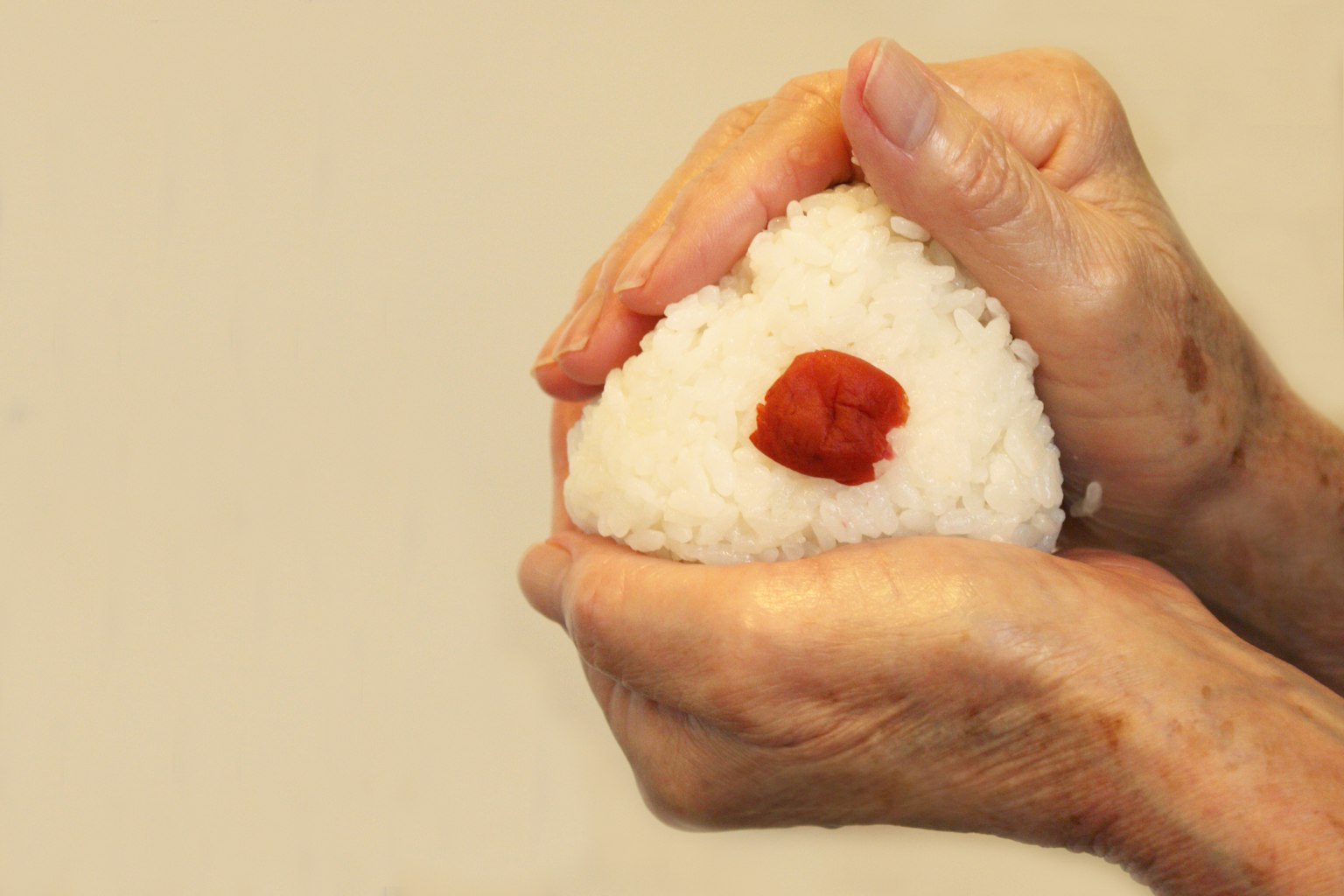 Une main tenant un onigiri avec une prune salée au centre