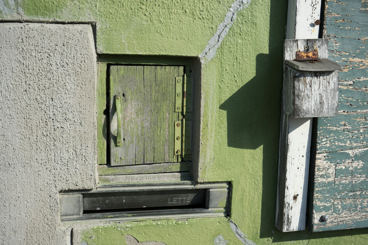 Immagine di una piccola porta in legno e di una cassetta postale su un muro verde