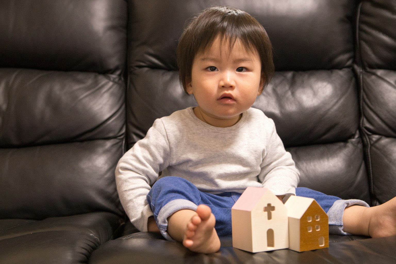 A boy sitting on a black sofa with wooden house toys