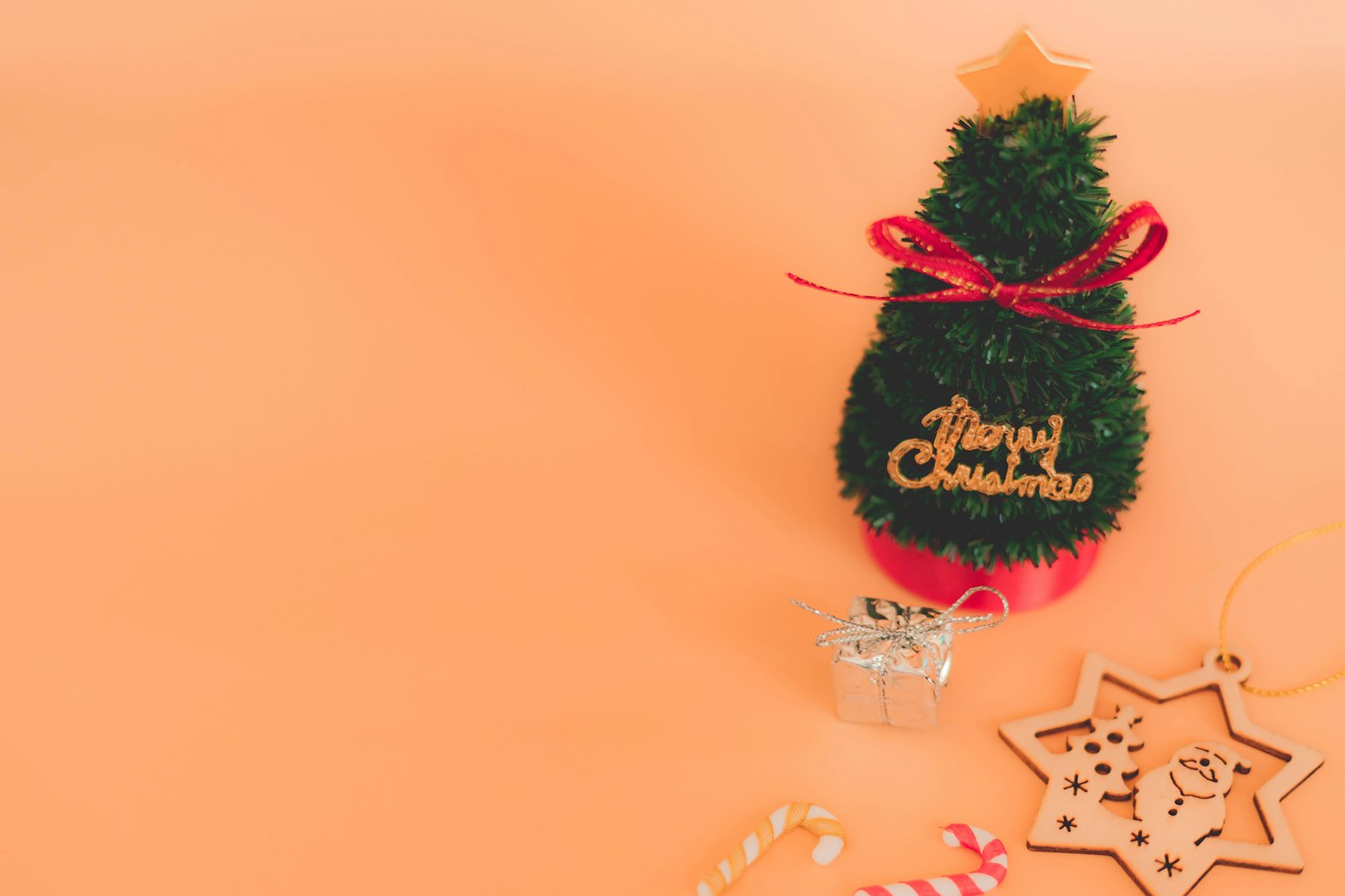 Ein kleiner Weihnachtsbaum mit Dekorationen und Geschenken auf einem Pfirsichhintergrund