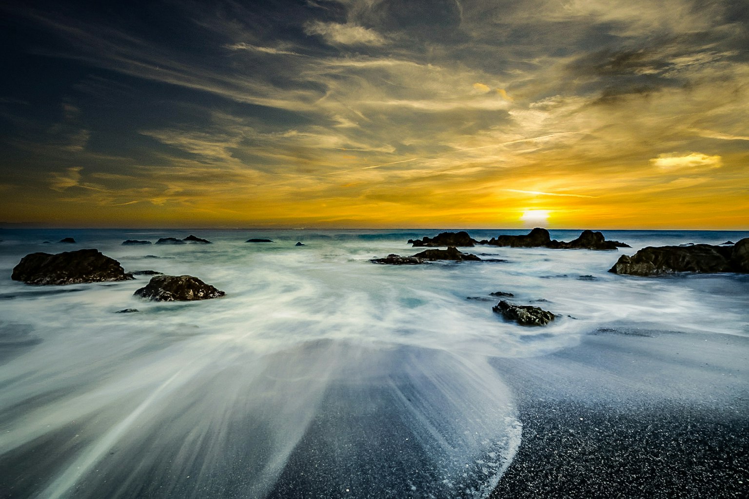 Atardecer costero con olas rompiendo contra las rocas