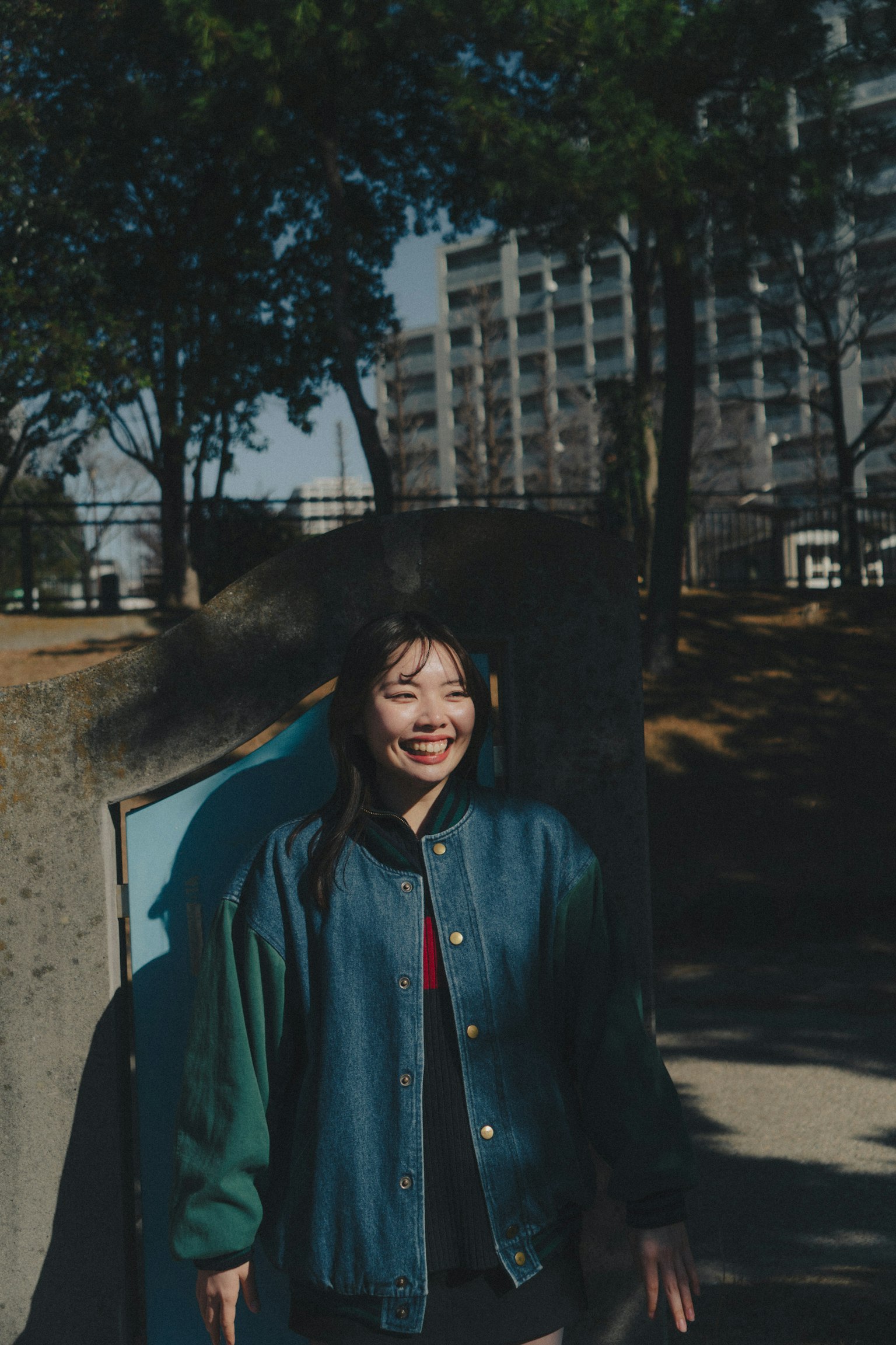 Eine Frau in einer blauen Jacke lächelt in einem Park