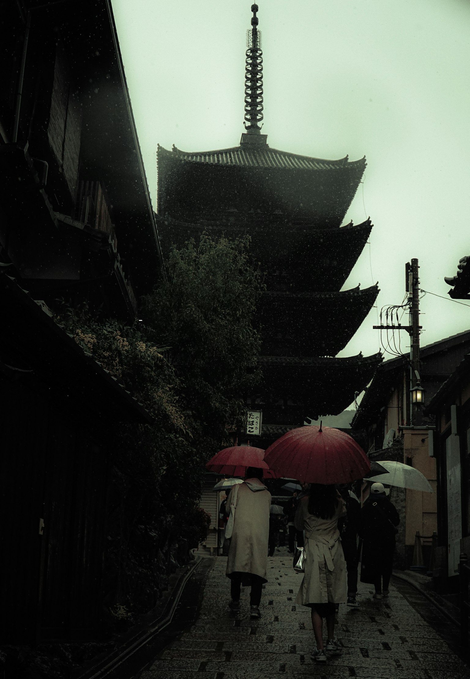Silhouette de personnes avec des parapluies près d'une pagode sous la pluie