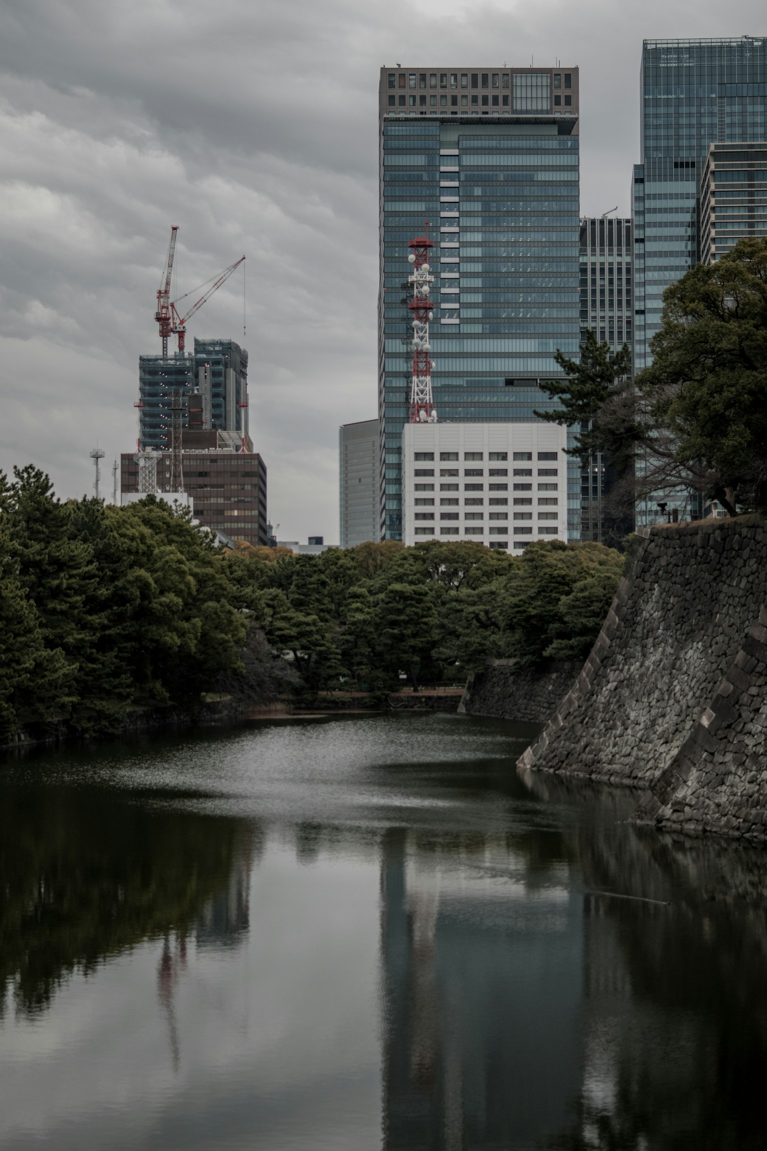 Paisaje urbano bajo cielos nublados con edificios reflejados en un río tranquilo y árboles verdes