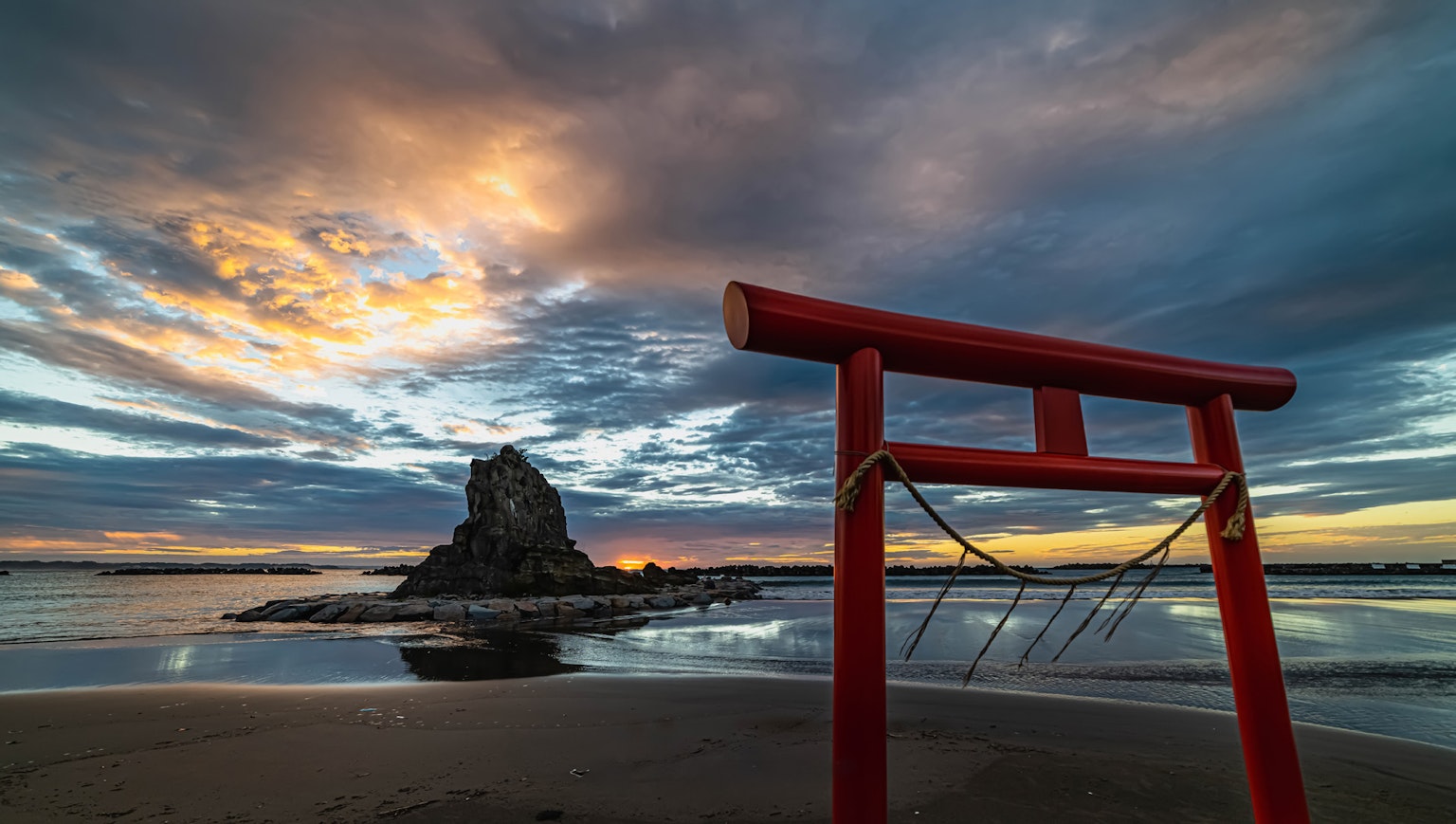 海滩上的红色鸟居和日落时的岩石岛