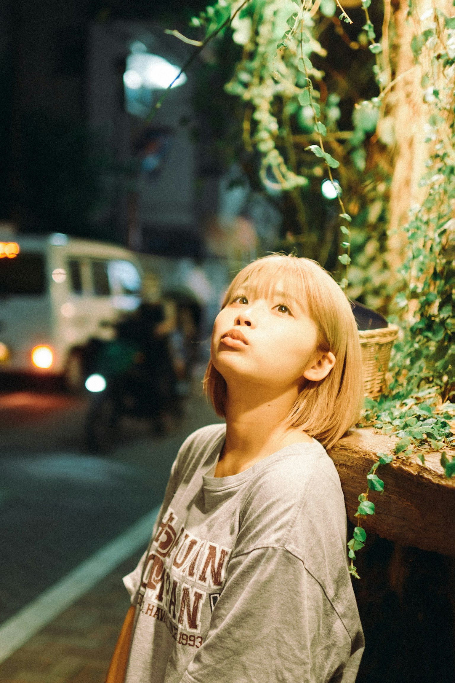 金发女性在夜间城市环境中仰望周围有绿色植物和汽车灯光