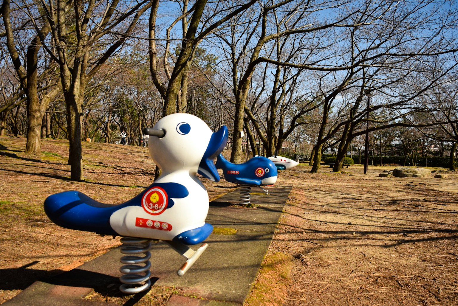 White robotic animal playground equipment in a park with bare trees