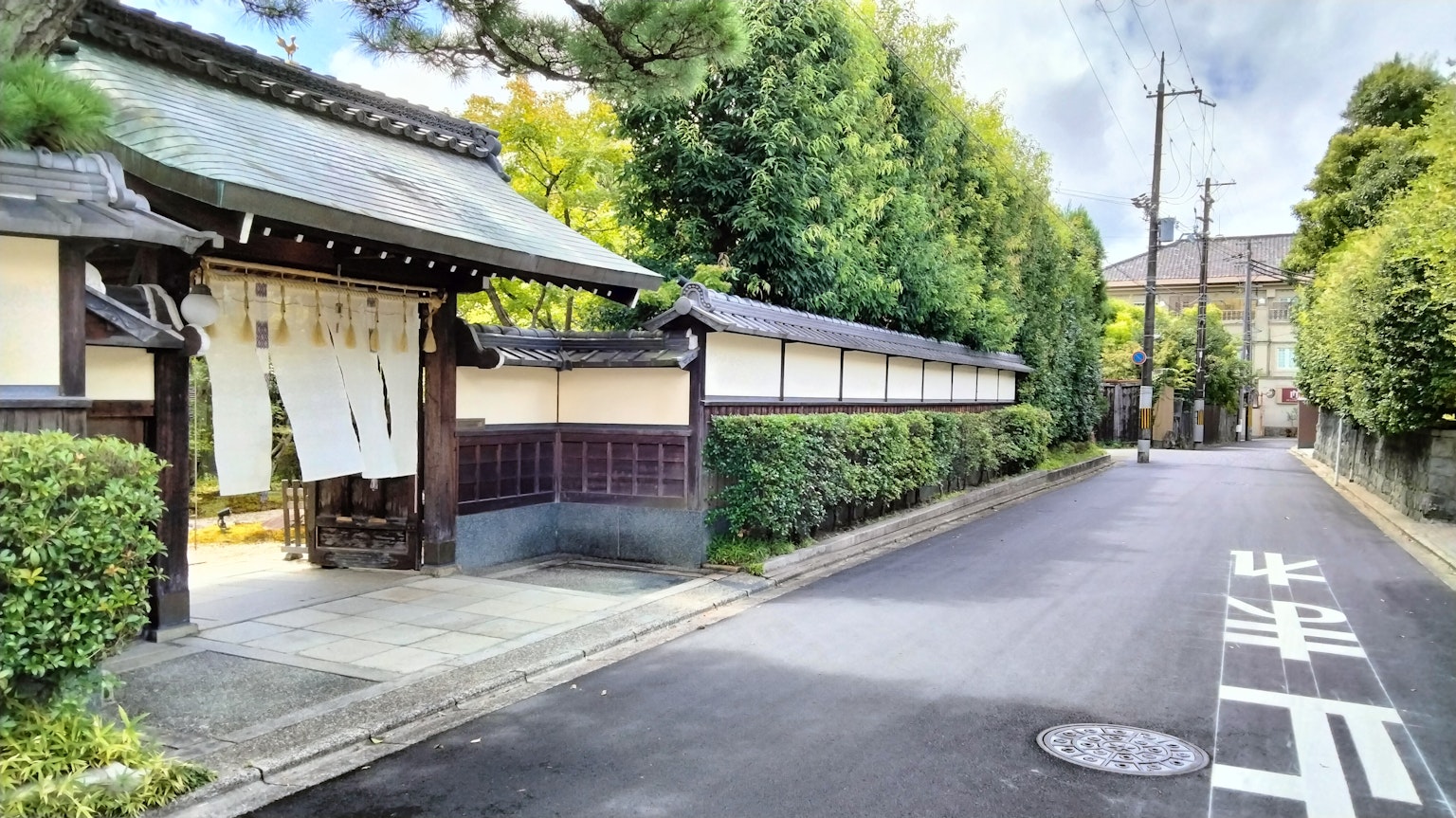 Quiet Japanese street with a traditional building entrance surrounded by lush greenery