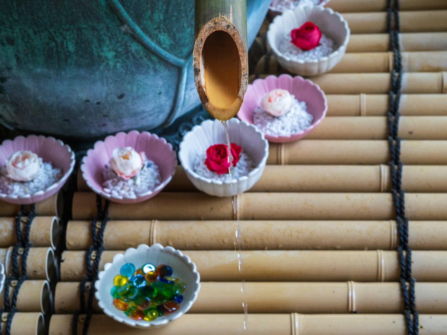 竹の上に置かれた小さな皿に花びらと宝石が並び、竹の筒から水が流れ落ちている