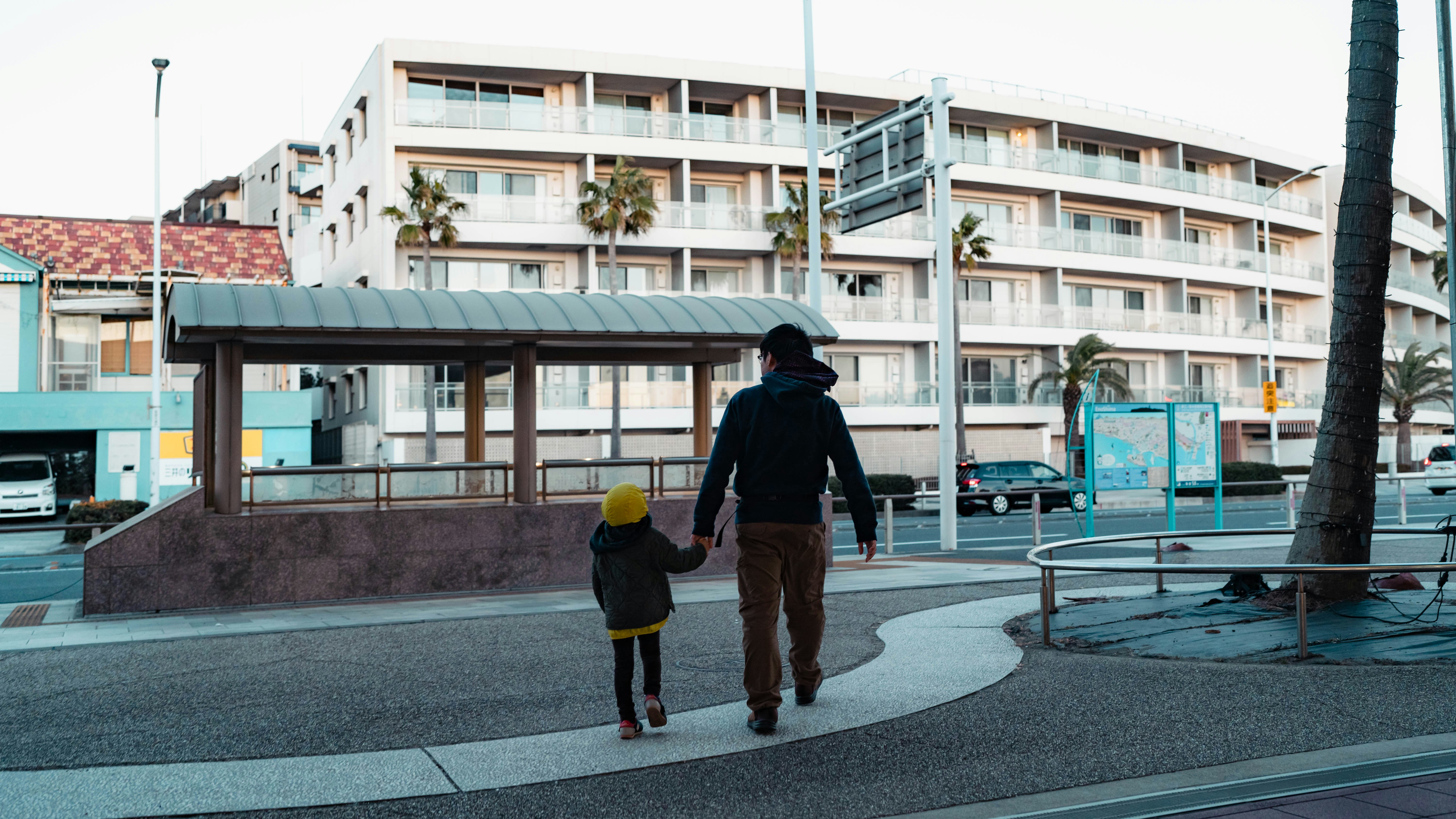 Parent and child holding hands walking at a residential intersection in front of apartments
