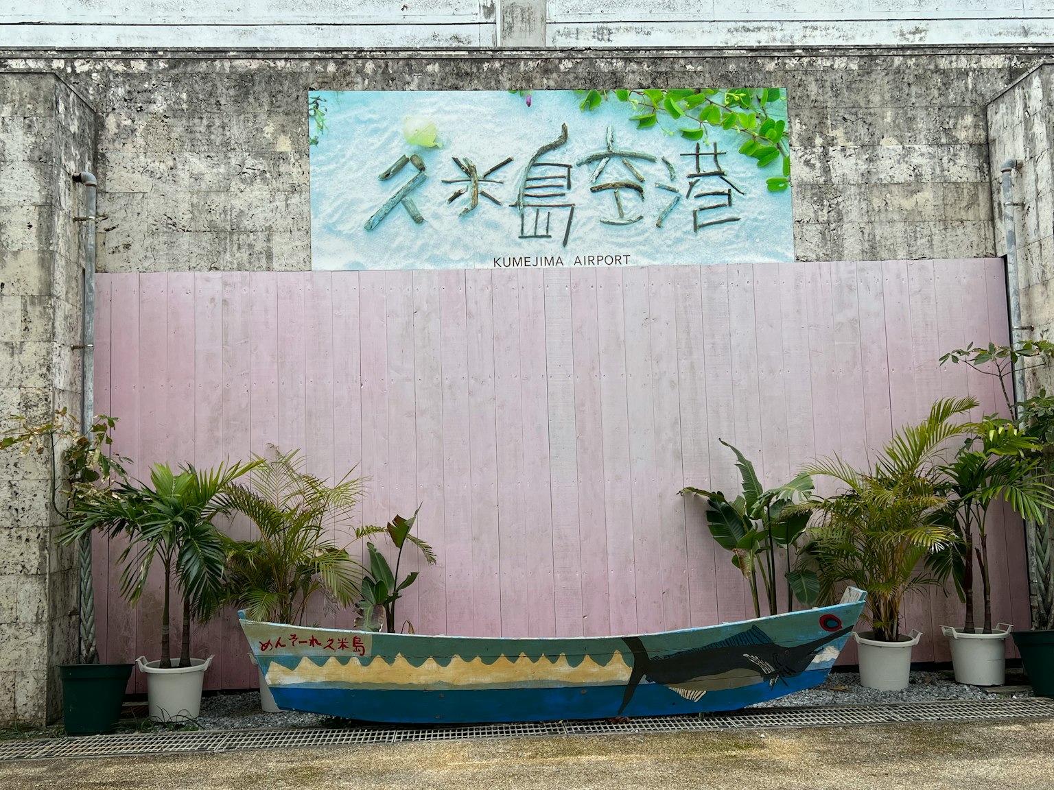 一艘色彩斑斕的船放置在有藍色字母標誌和綠色植物的牆前