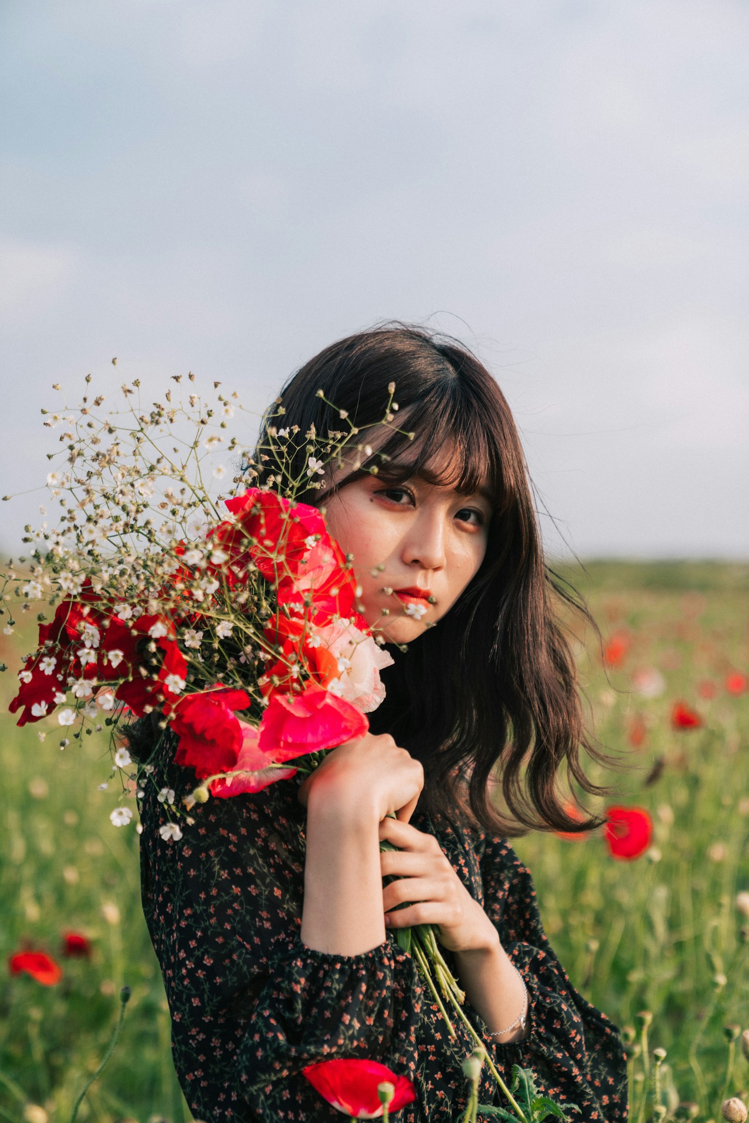 Porträt einer Frau mit einem Strauß roter Blumen in einem Feld mit Wildblumen