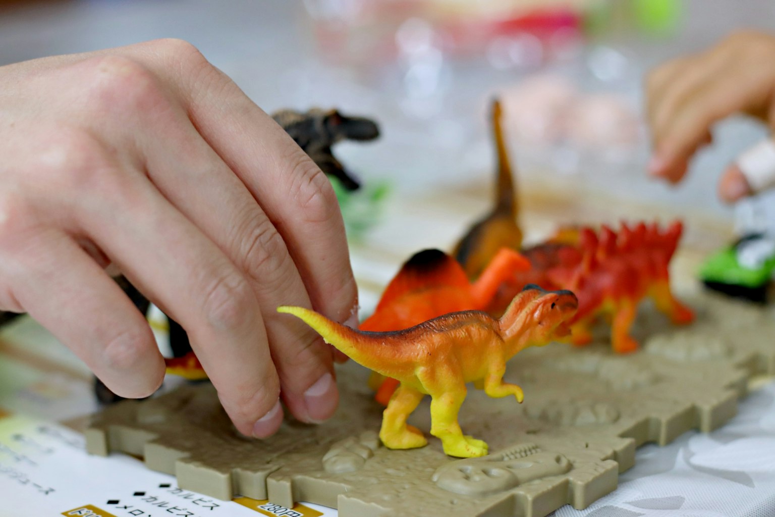 Une main manipulant des jouets dinosaures colorés sur un tapis de jeu