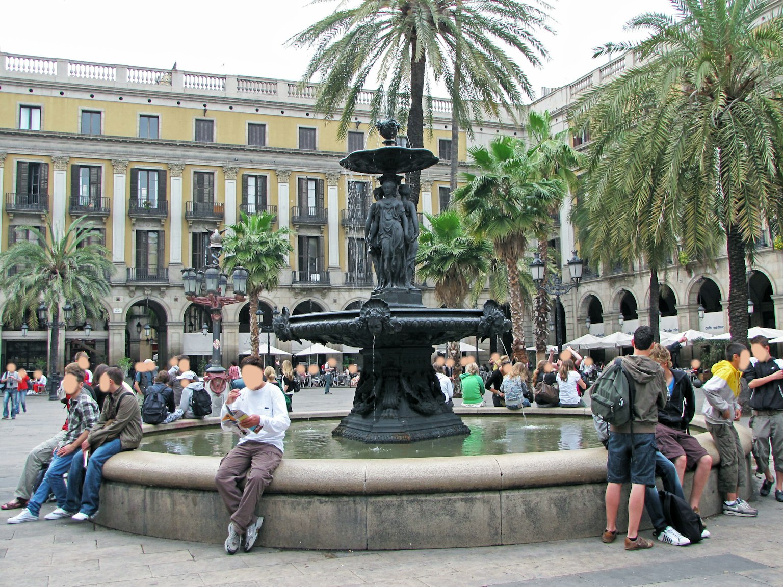 Fontaine dans une place de Barcelone entourée de palmiers et de personnes assises