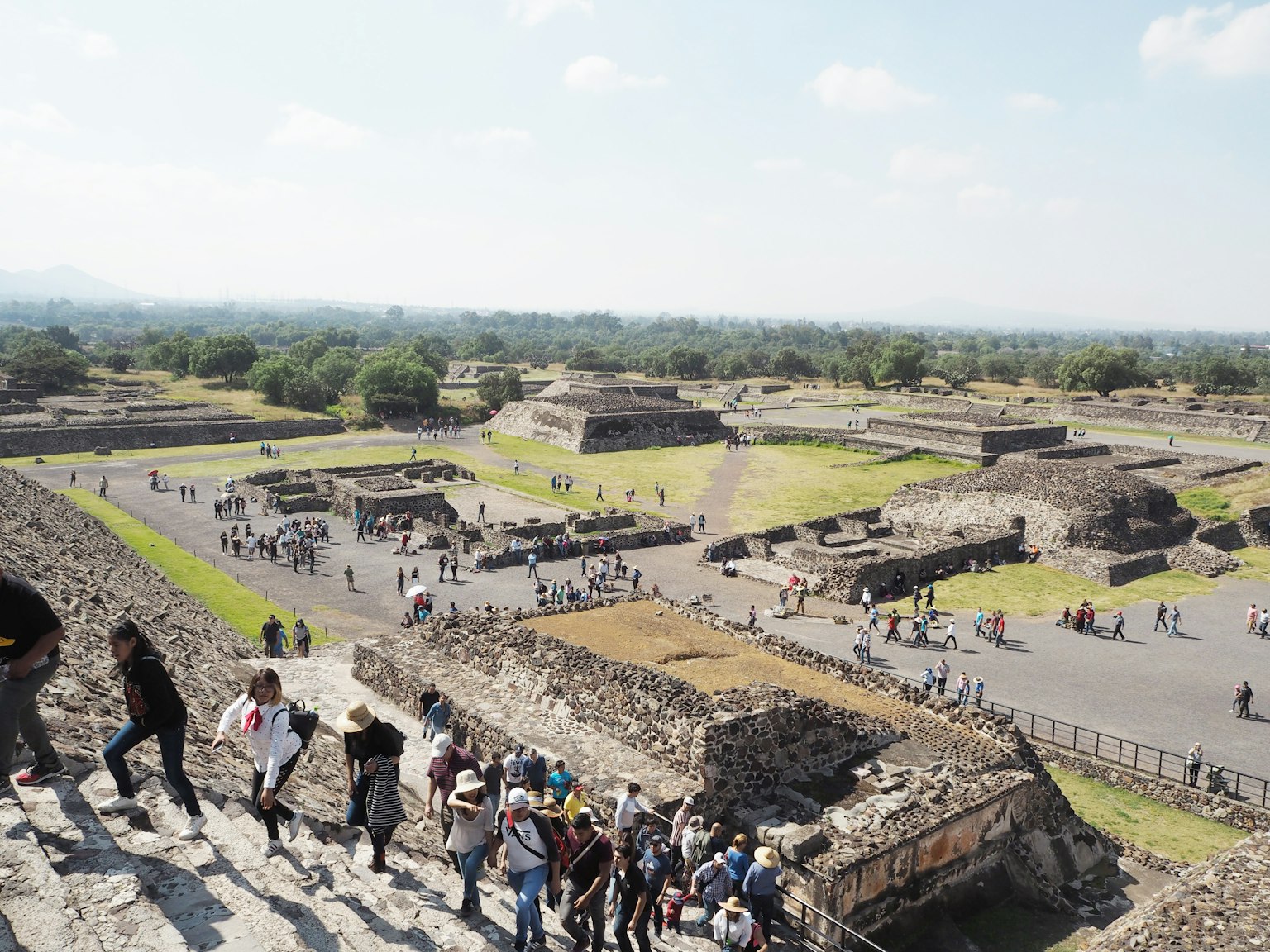 Visitatori che salgono le scale a Teotihuacan con piramidi sullo sfondo