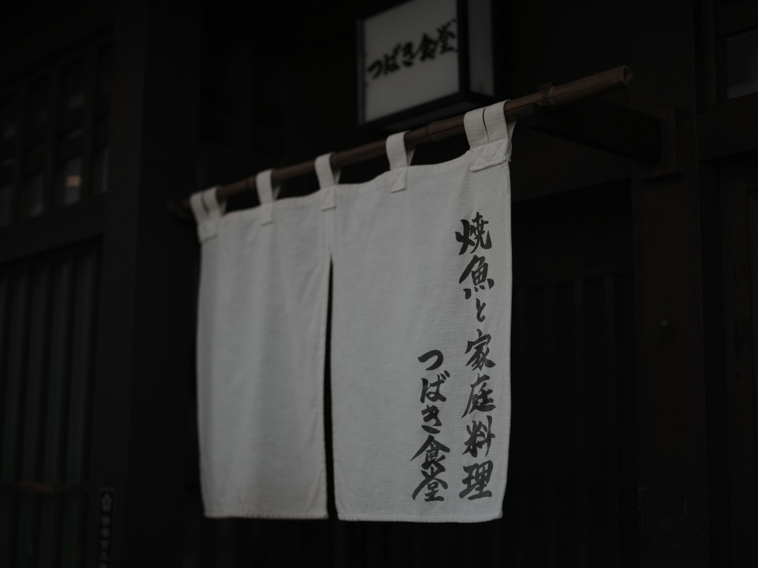 Tirai noren tradisional Jepang dengan karakter kanji di pintu masuk restoran