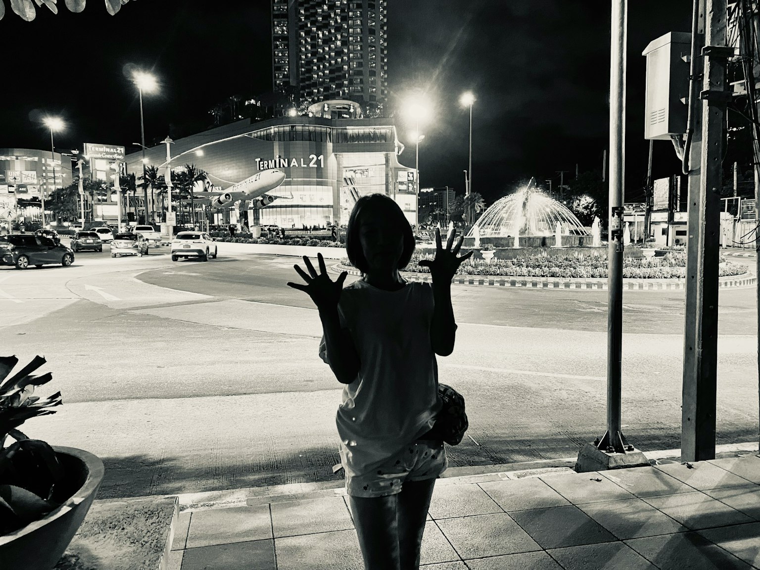 Silhouette einer Person mit erhobenen Händen an einer nächtlichen Straßenecke mit hellen Gebäuden im Hintergrund