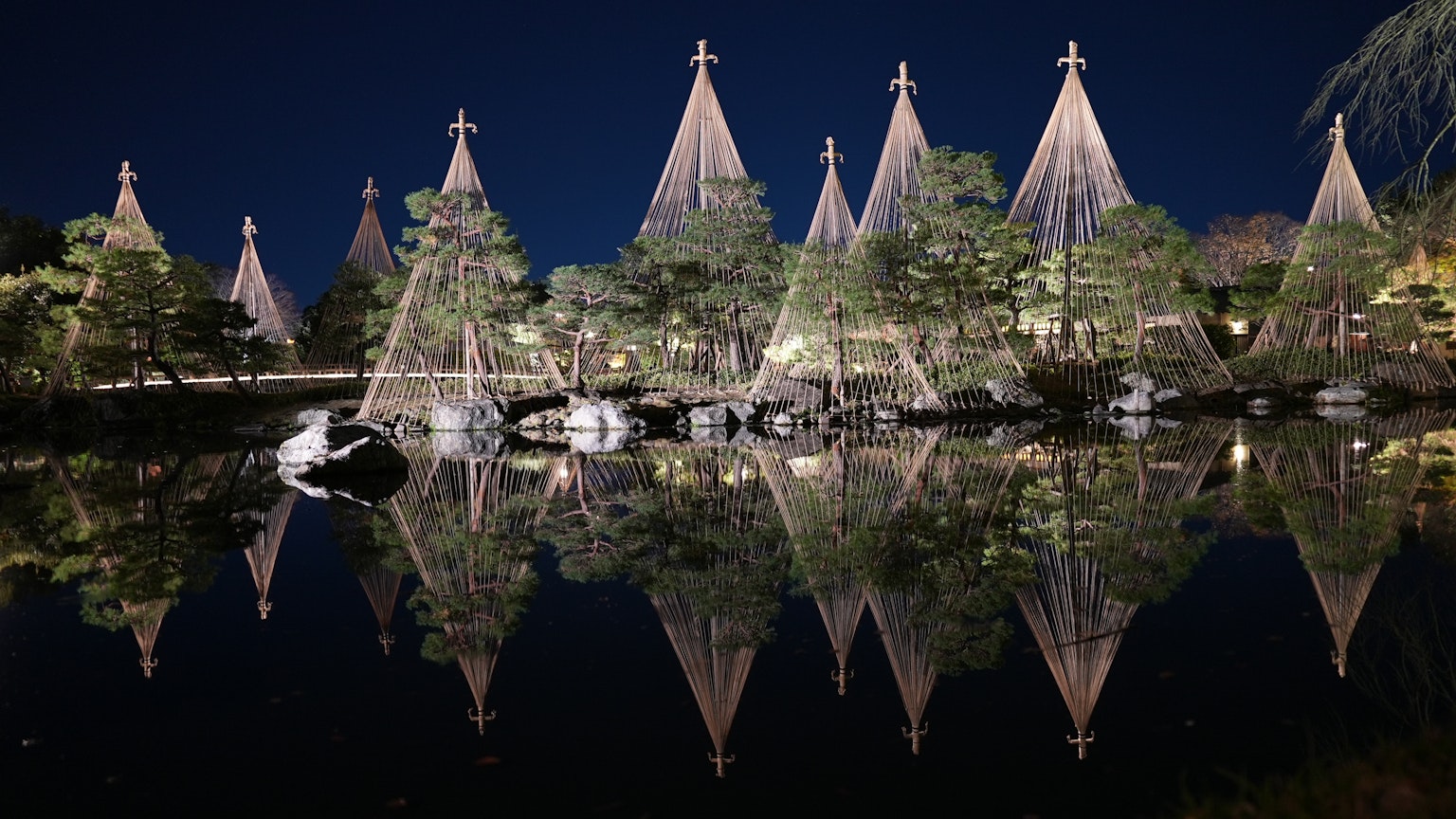 夜の池に映る美しい日本庭園の松の木と伝統的な竹の支柱