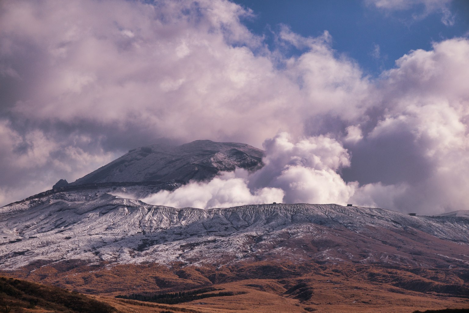 Paisaje volcánico cubierto de nieve con nubes dramáticas