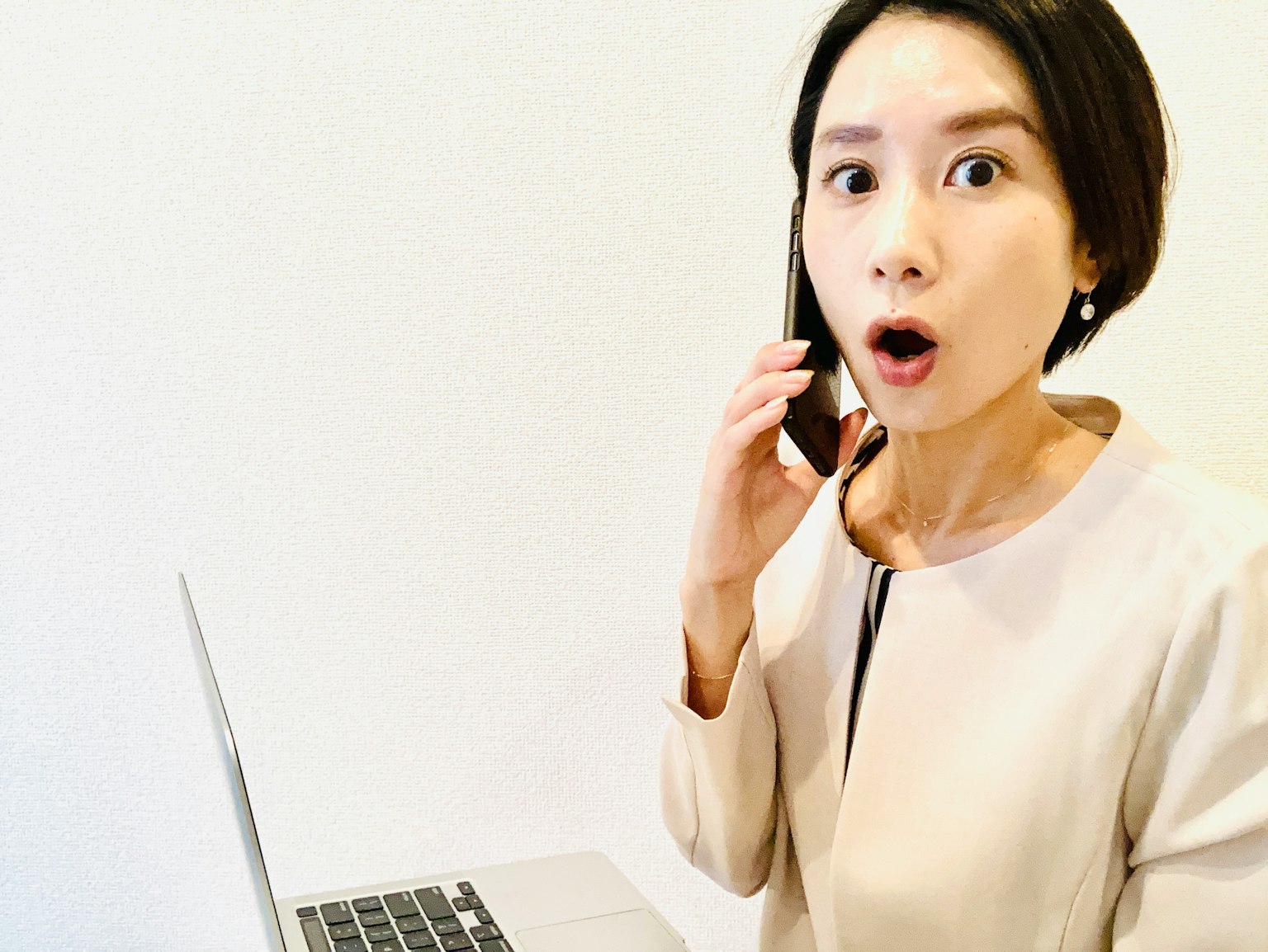 Seorang wanita terkejut memegang telepon sambil melihat laptop