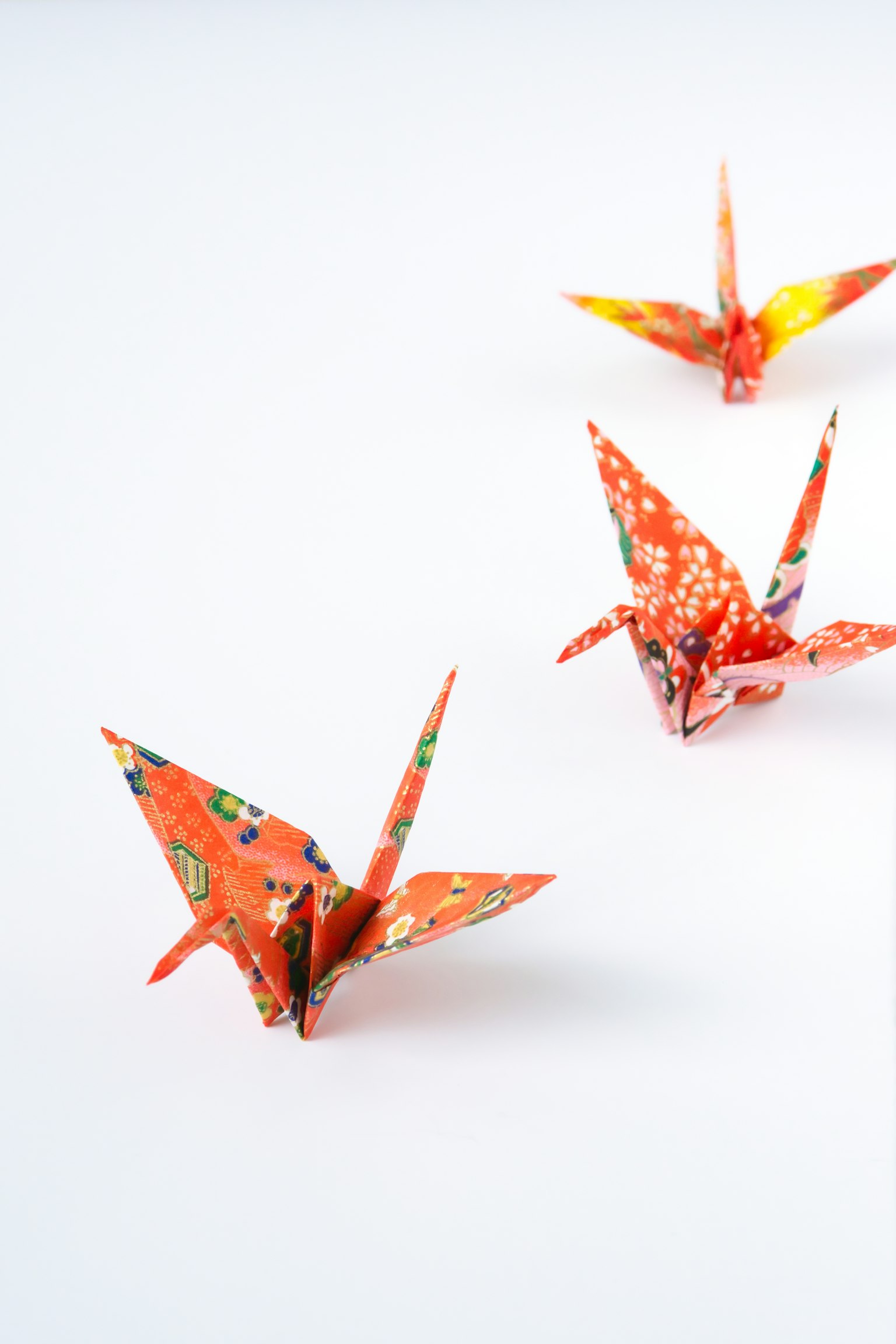 Tres grúas de origami naranjas dispuestas sobre un fondo blanco