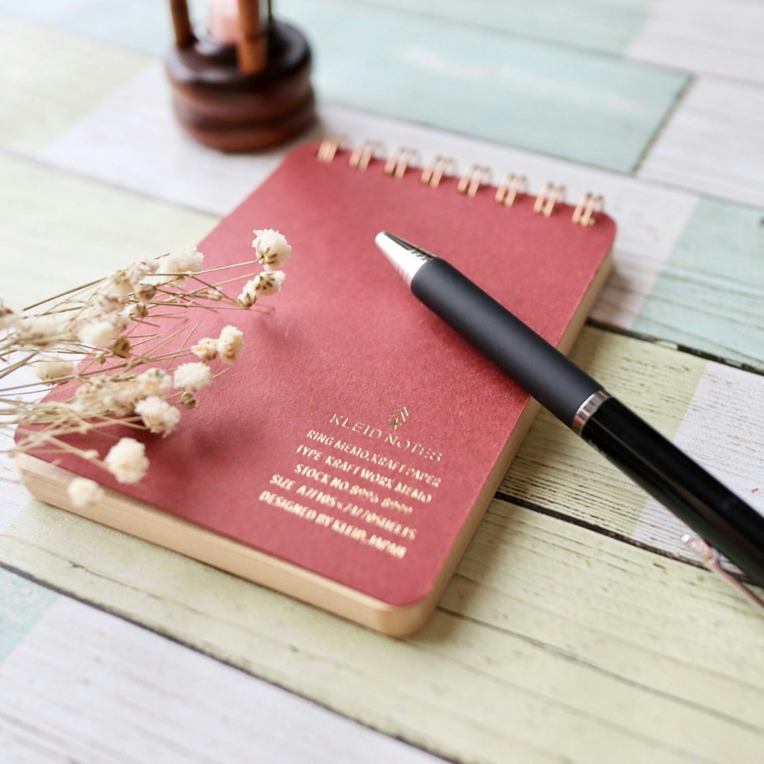 Un cuaderno rojo y un bolígrafo negro sobre una mesa de madera