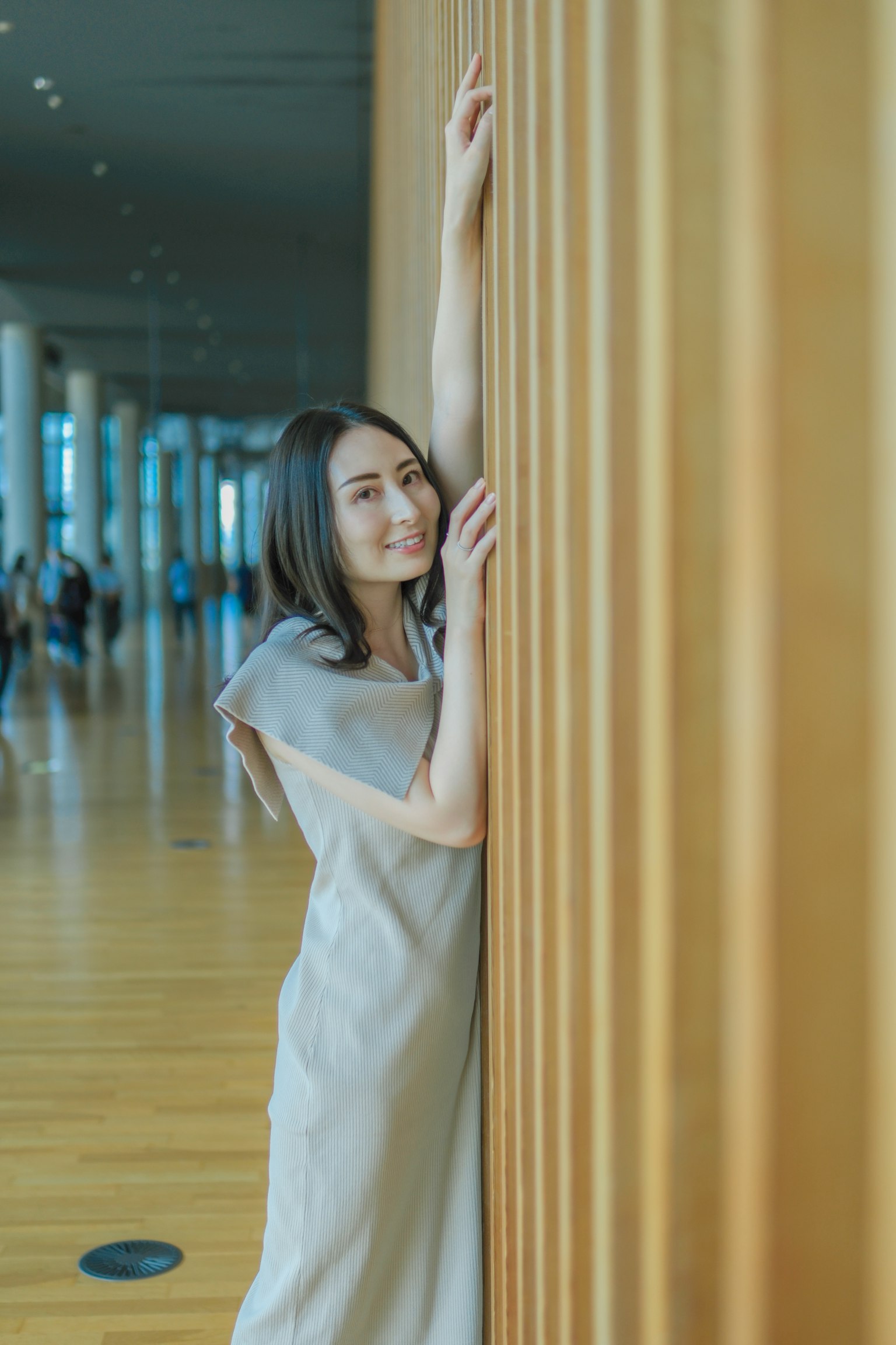 一位女性微笑着靠在室内的木墙上