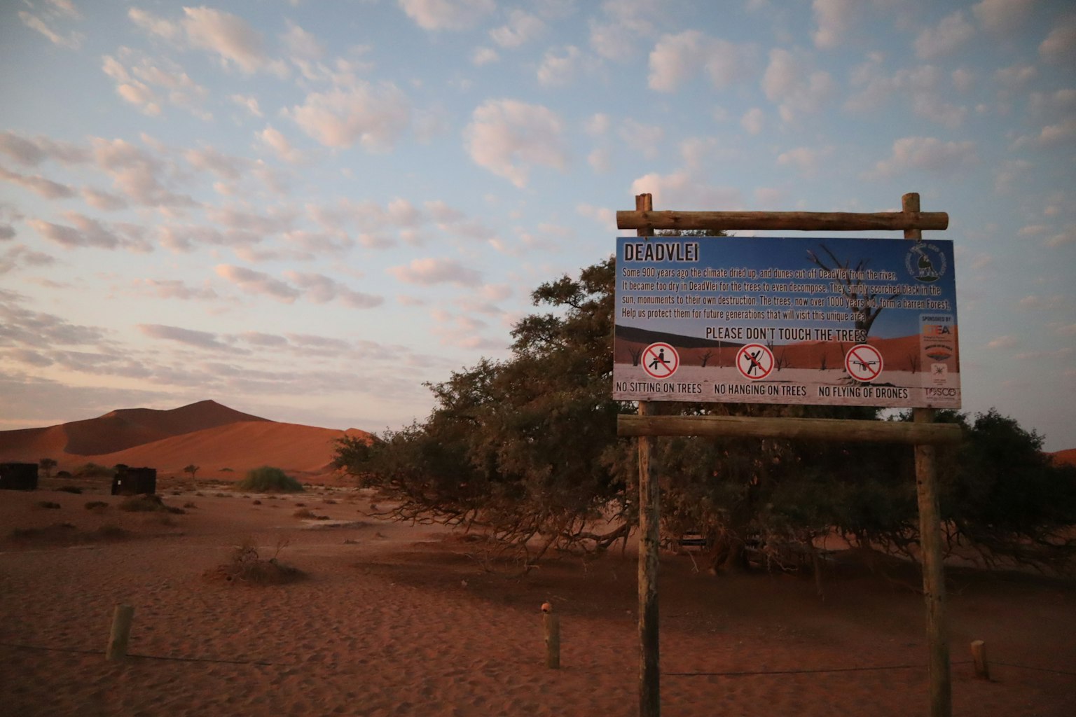 Cartello informativo in un paesaggio desertico con cielo blu e nuvole illuminate dal tramonto