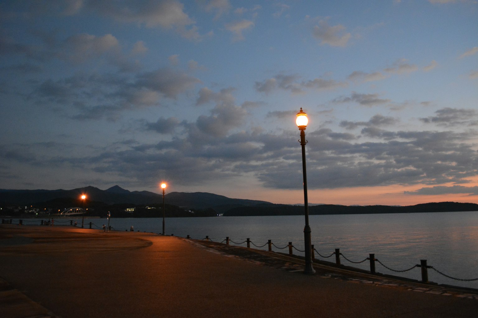 Escena de lago al atardecer con un farola a lo largo de un paseo y agua tranquila